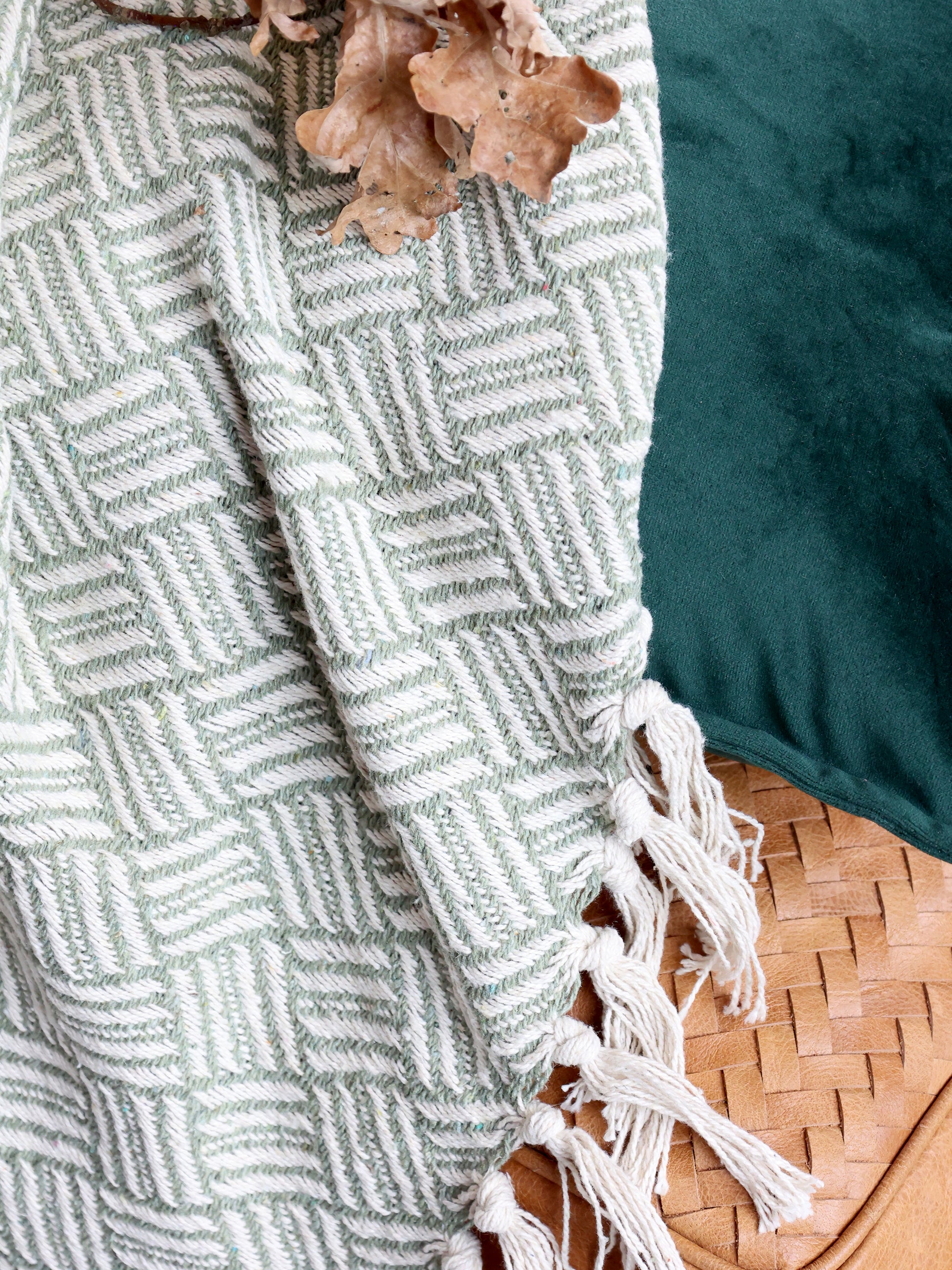 Textured green blanket with white geometric pattern and tassels on a surface.