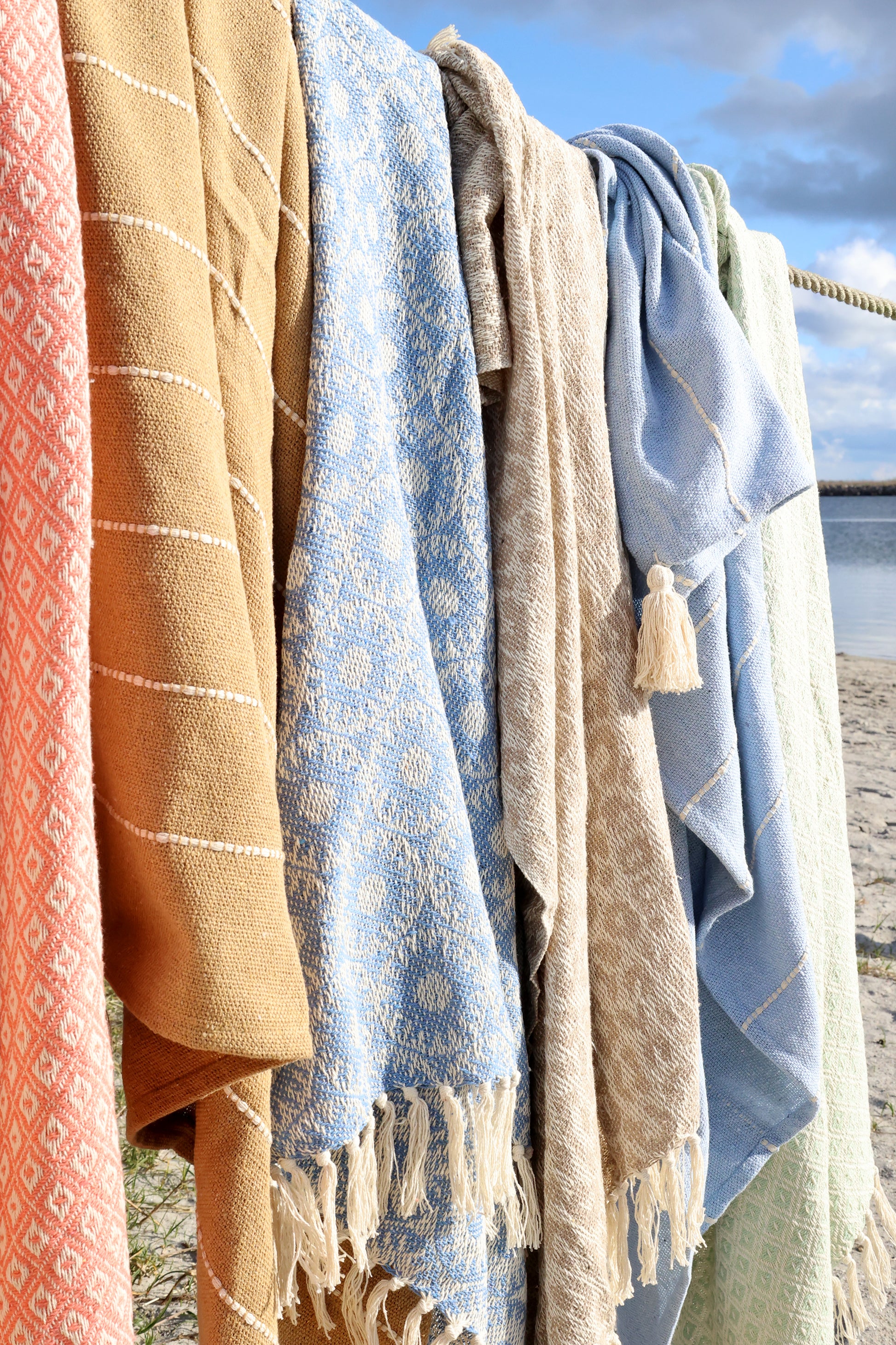 Collection of colorful towels hanging on a line with a beach in the background