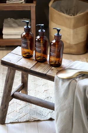 Three brown bottles with black pumps on a wooden stool in a home setting.