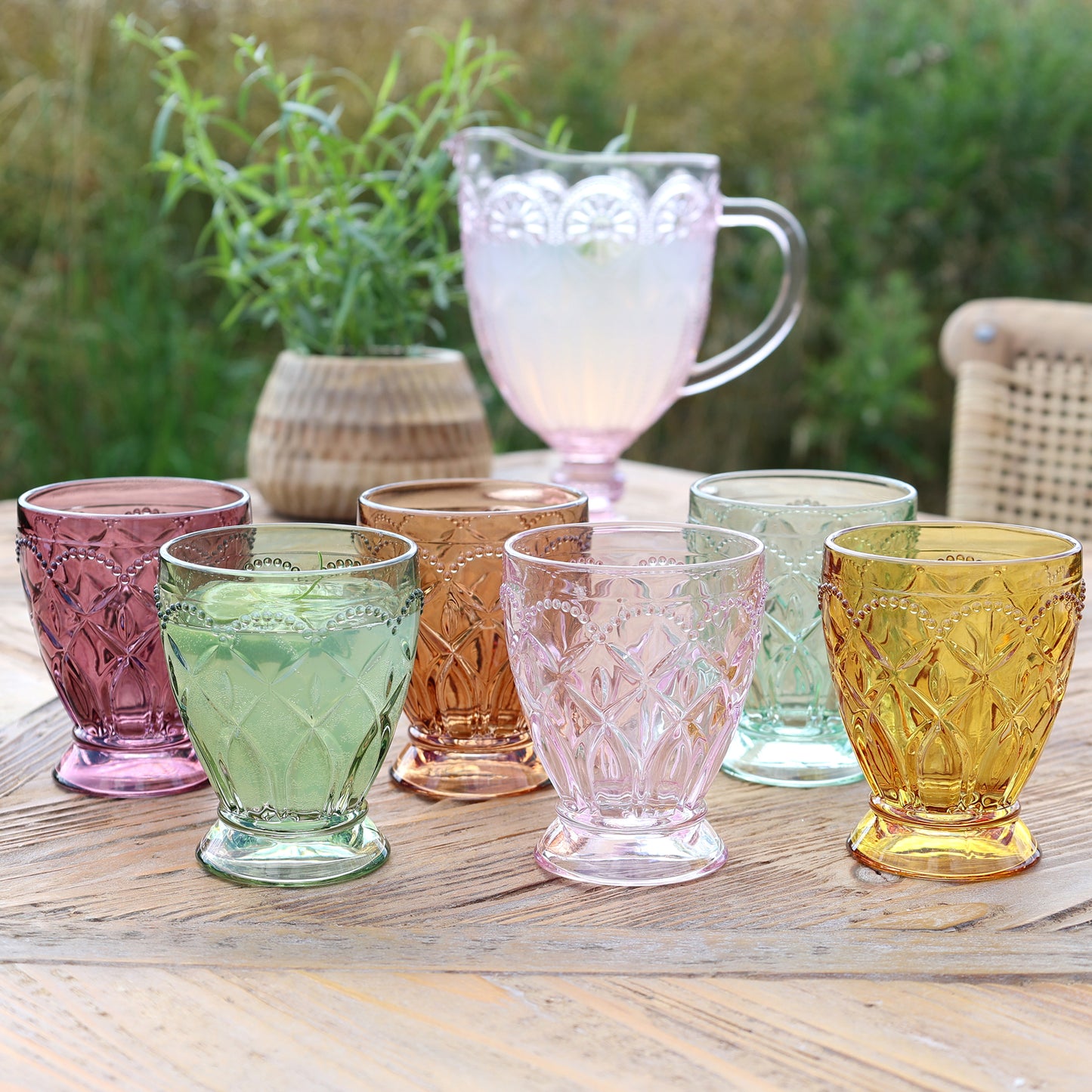 Set of colorful glass tumblers on a wooden surface with a blurred natural background