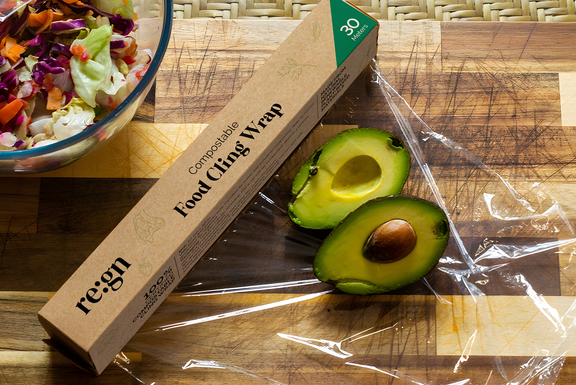 Avocado halves on a cutting board with a box of 're:gn' compostable food cling wrap.