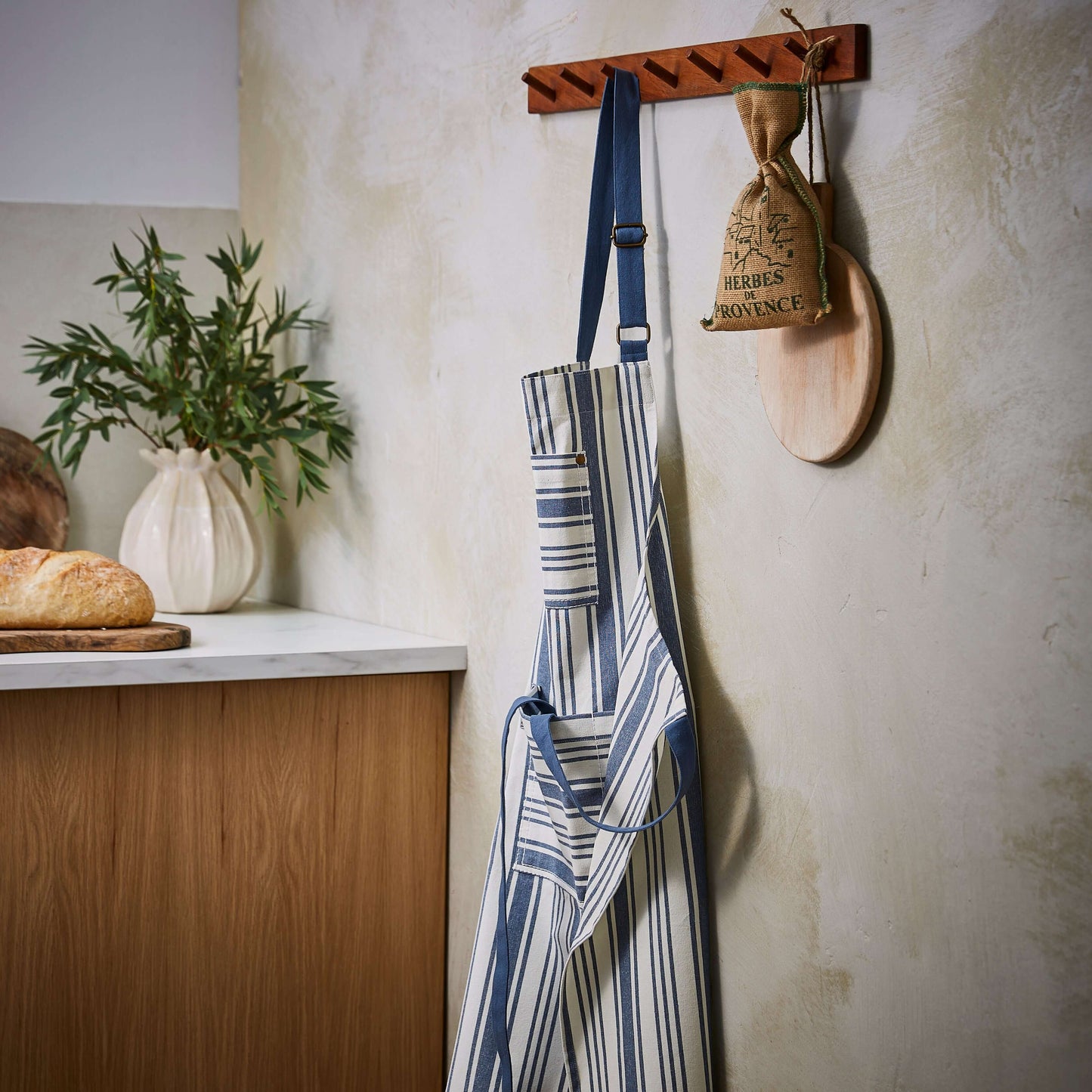 Kitchen scene with apron, plant, and wooden utensil holder on a textured wall.