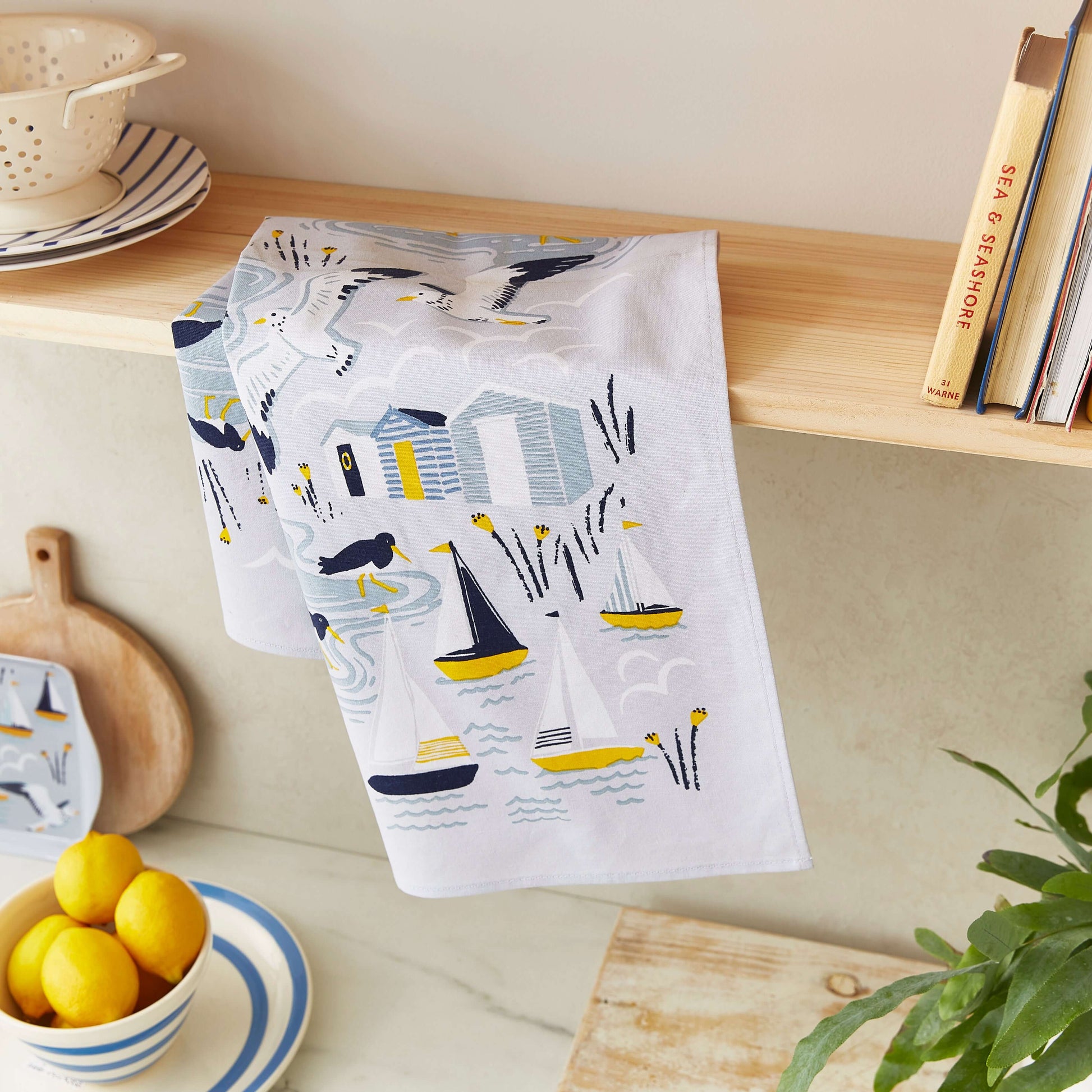 Tea towel with nautical design on a kitchen shelf with lemons and books.