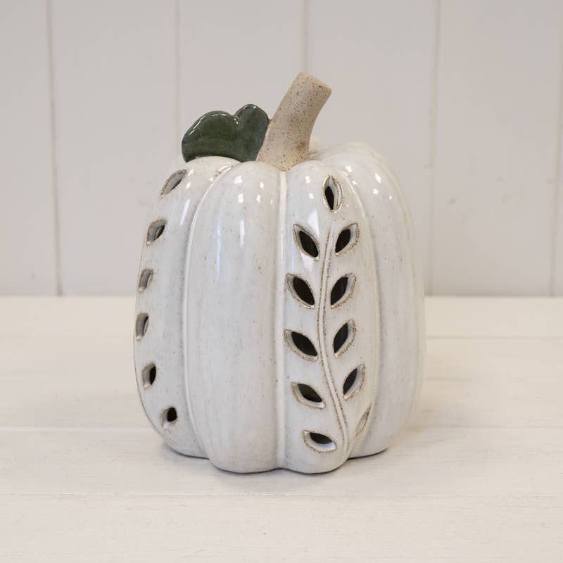 A decorative ceramic pumpkin figurine in a glossy off-white glaze, featuring leaf-shaped cutouts on the sides, a textured beige stem, and a small dark green leaf accent at the top, set against a white paneled background.