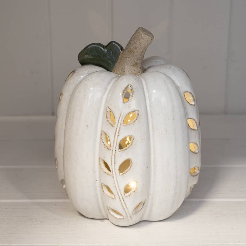 A white ceramic decorative pumpkin with gold leaf accents and a dark green stem, set against a white paneled background.