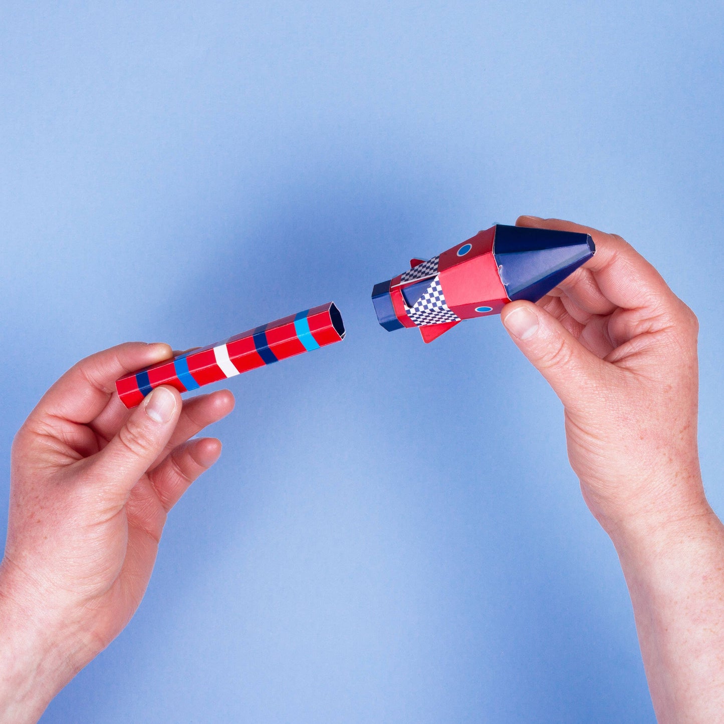 Two hands holding a red and blue rocket toy against a light blue background