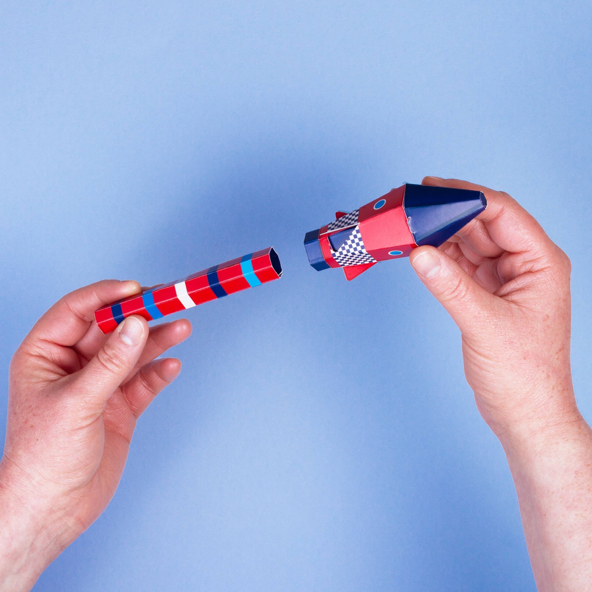 Two hands holding a red and blue rocket toy against a light blue background