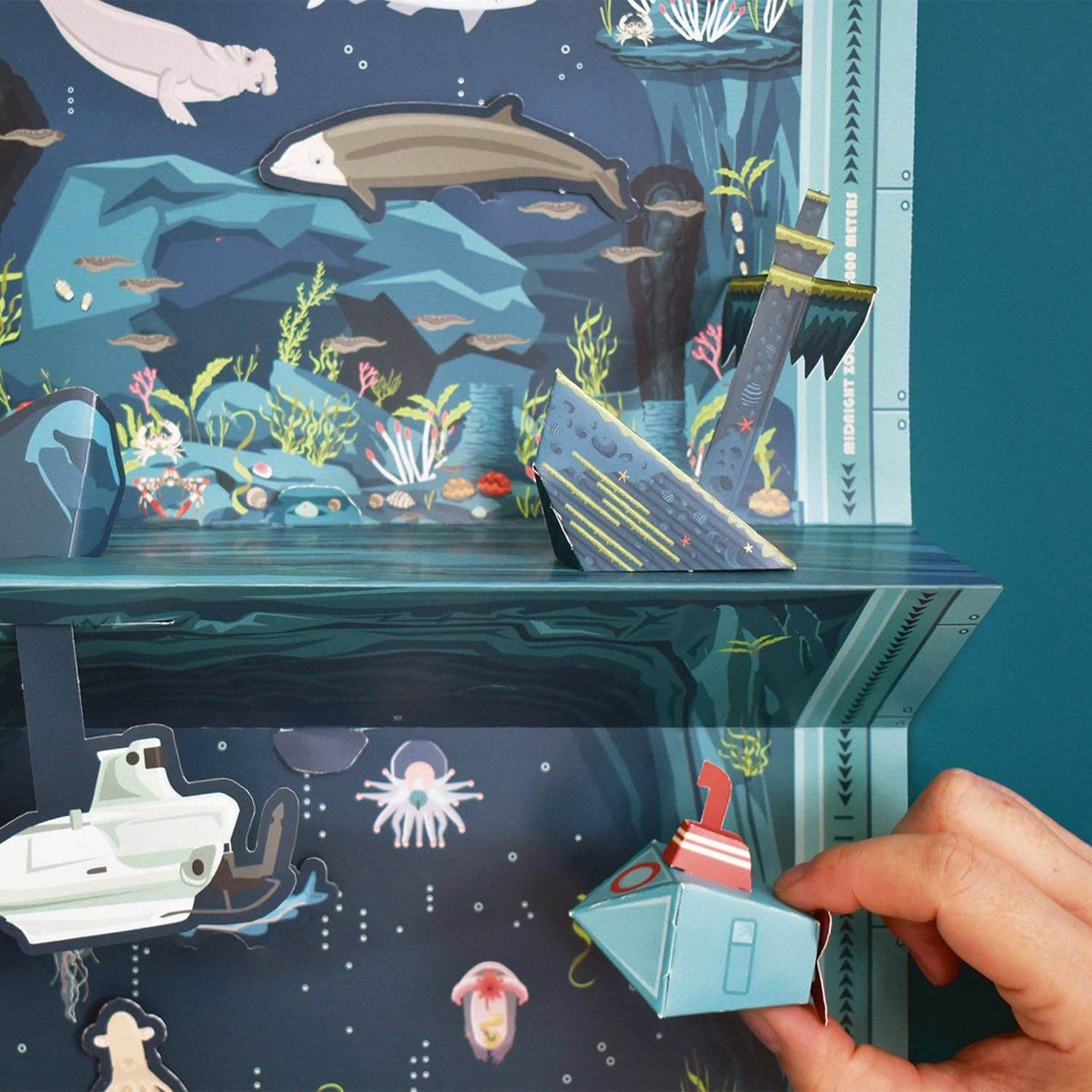 Underwater scene with a hand holding a small boat model, surrounded by marine life and a submarine.
