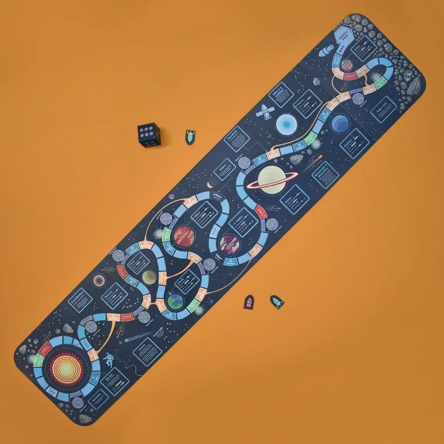 A long rectangular board game with a space-themed design, shown diagonally on a solid orange background. The board features a dark blue outer-space pattern with colorful winding tracks, planets, stars, and small printed game panels.