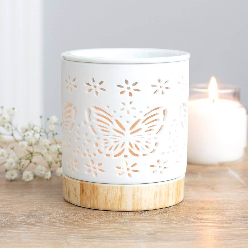 White ceramic lantern with butterfly design on a wooden base, placed on a wooden surface with a blurred background.