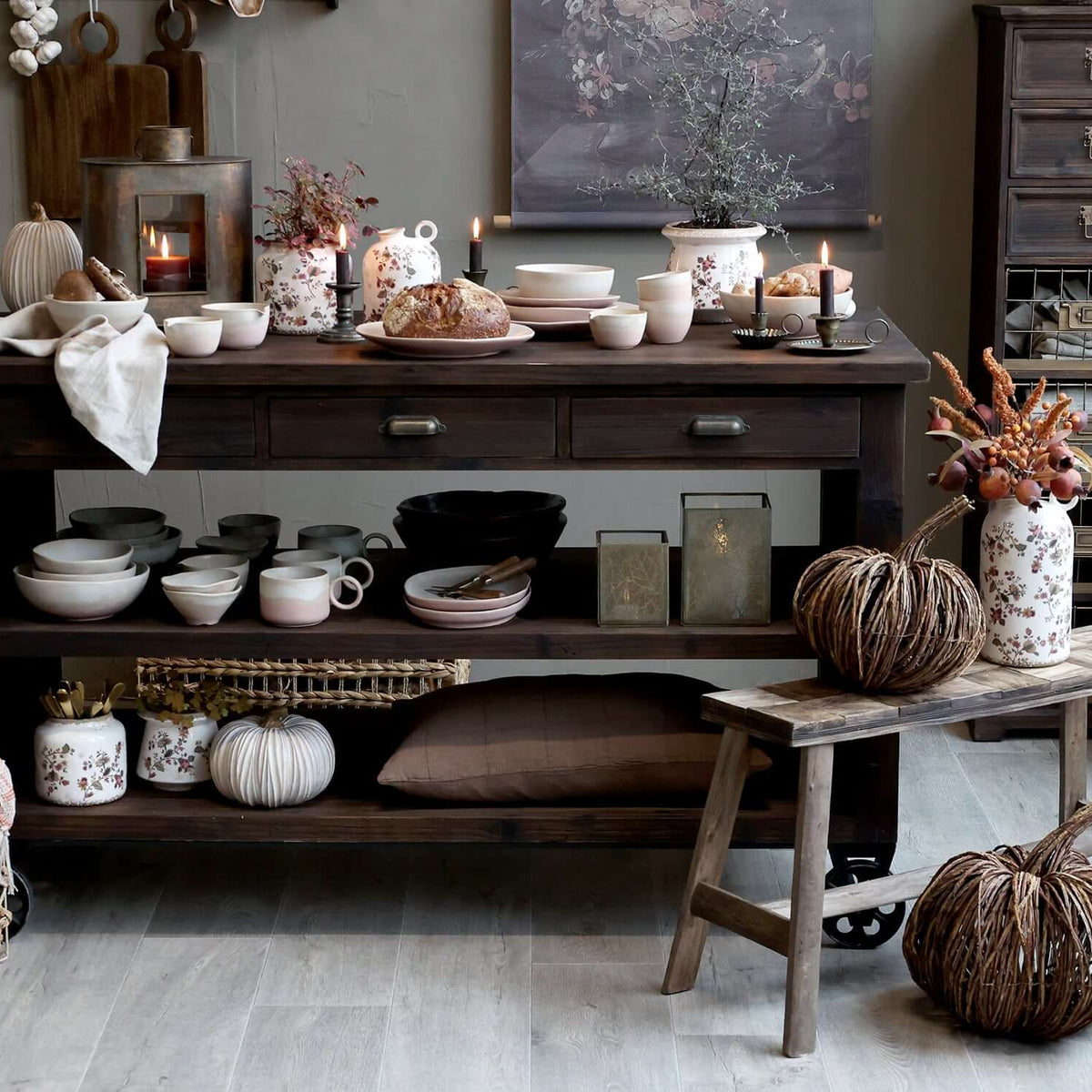 Decorative setting with a wooden console table, candles, and pumpkins in a room.
