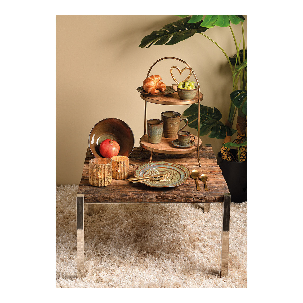 Decorative table setting with a two-tiered tray, plates, cups, and a plant in the background.