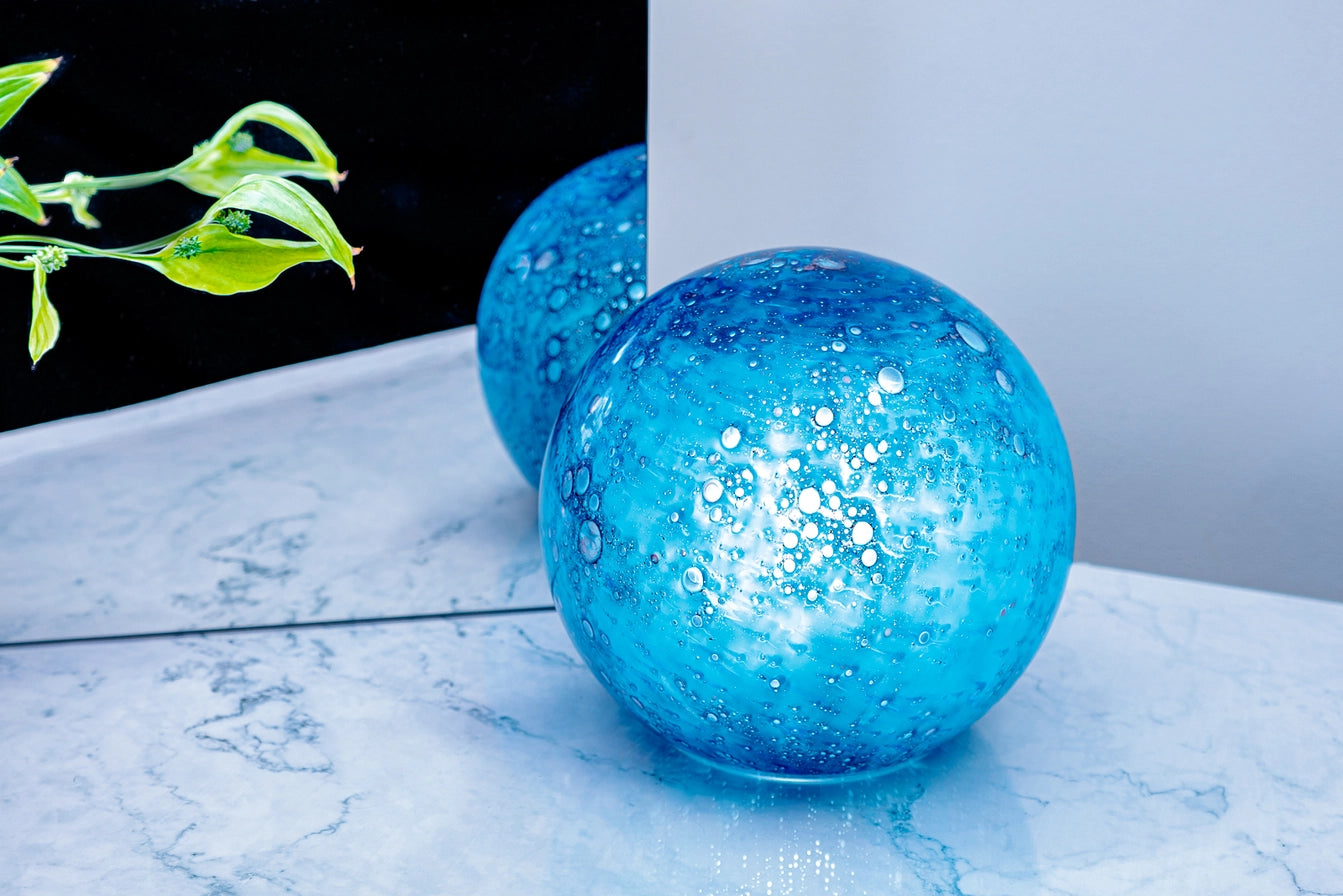 Blue glass lamp on a marble surface with a plant in the background