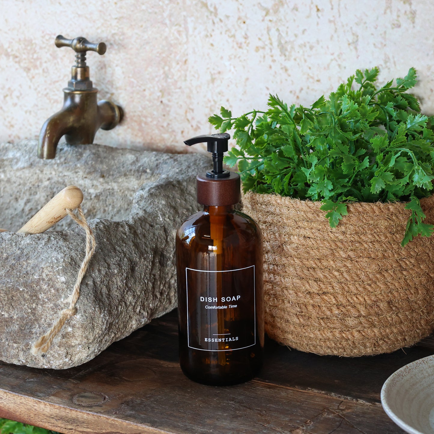 mocca glass dish soap pump bottle displayed on a countertop with a rustic sink and greenery background.