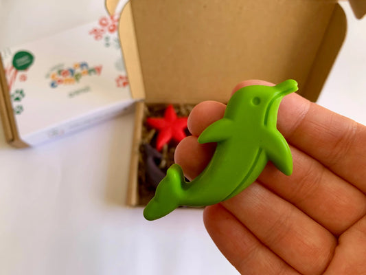 Green dolphin-shaped natural crayon held in a hand with a blurred background