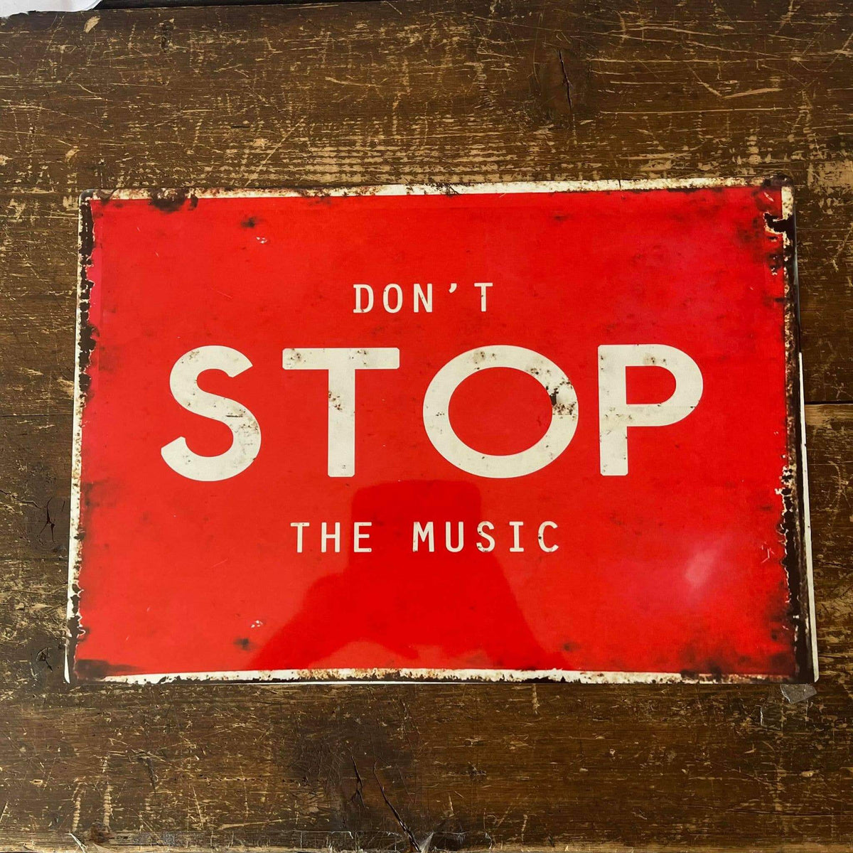 Red sign with 'Don't Stop The Music' text on a textured surface