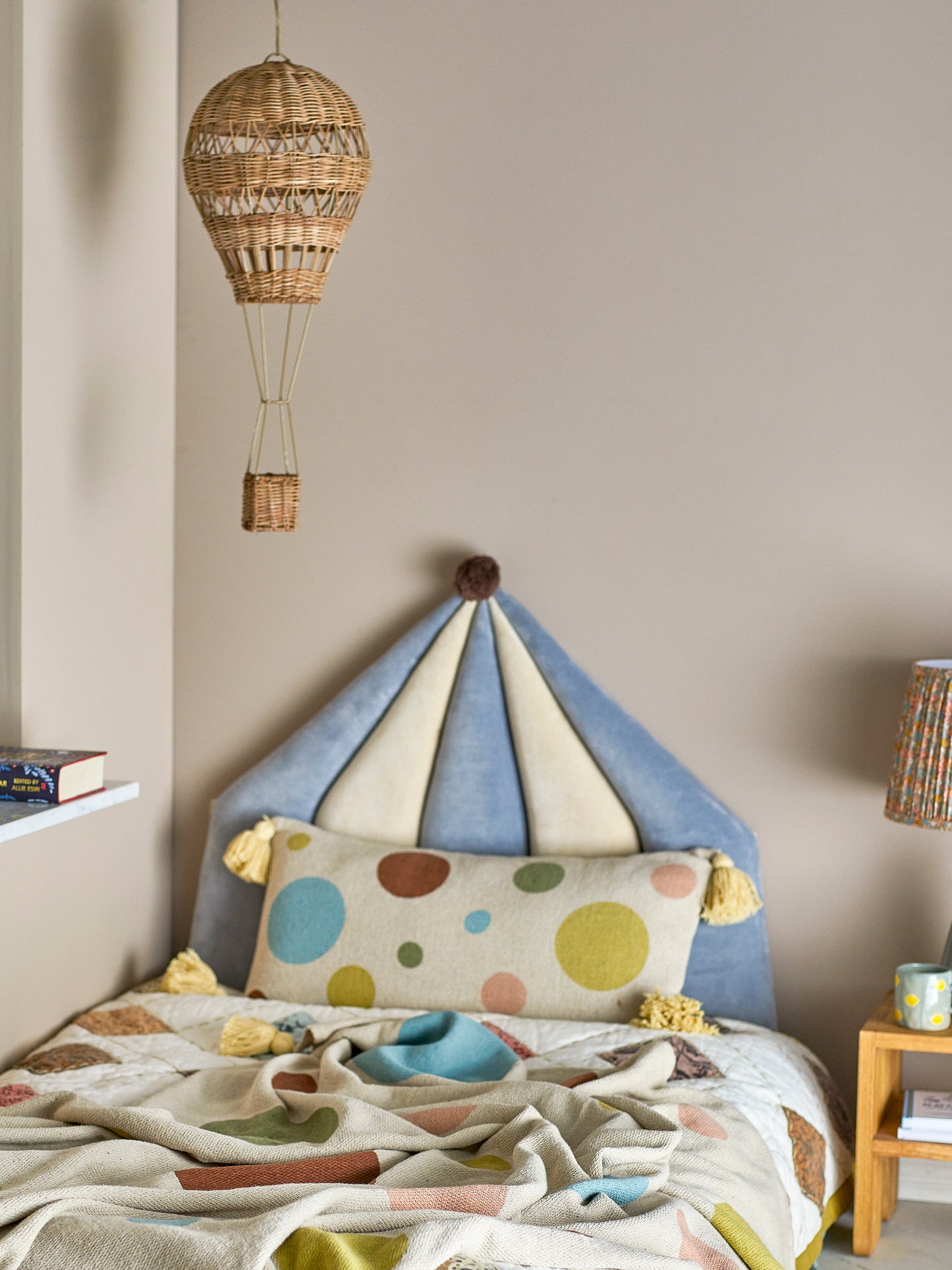 Children's bedroom with a colorful bed canopy, polka dot pillow, and hanging woven basket.