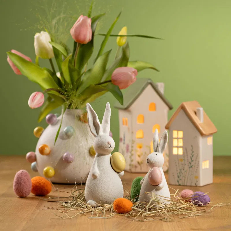 Decorative scene with Easter-themed items including rabbits, eggs, and a vase with flowers on a wooden surface.