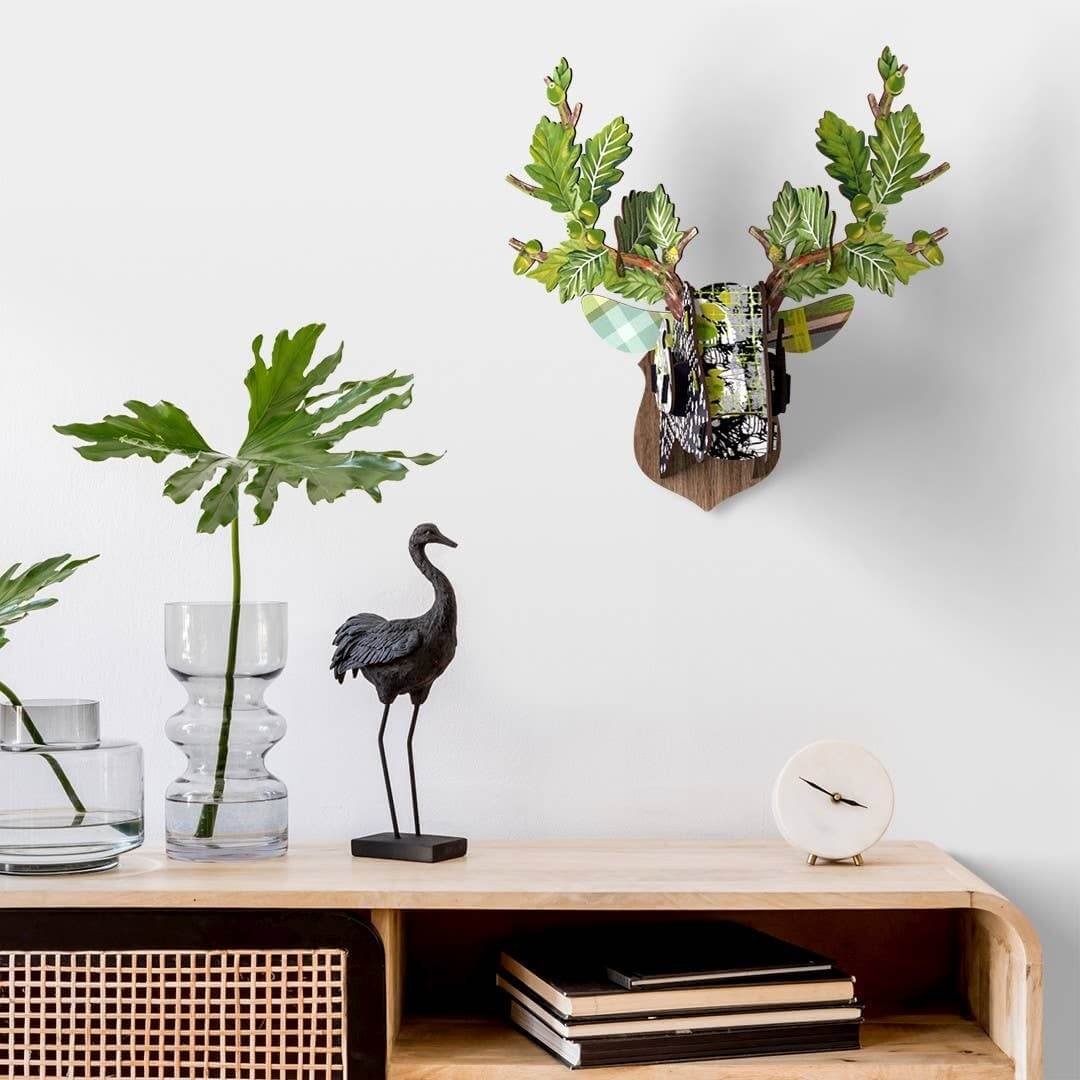 A decorative stag head wall art with a floral pattern in black, white, and green, featuring branch, oak leaf, and acorn effects.