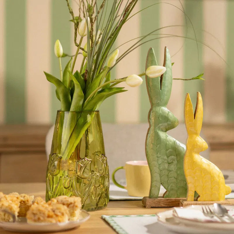Decorative table setting with a vase of flowers, rabbit figurines, and a cup.