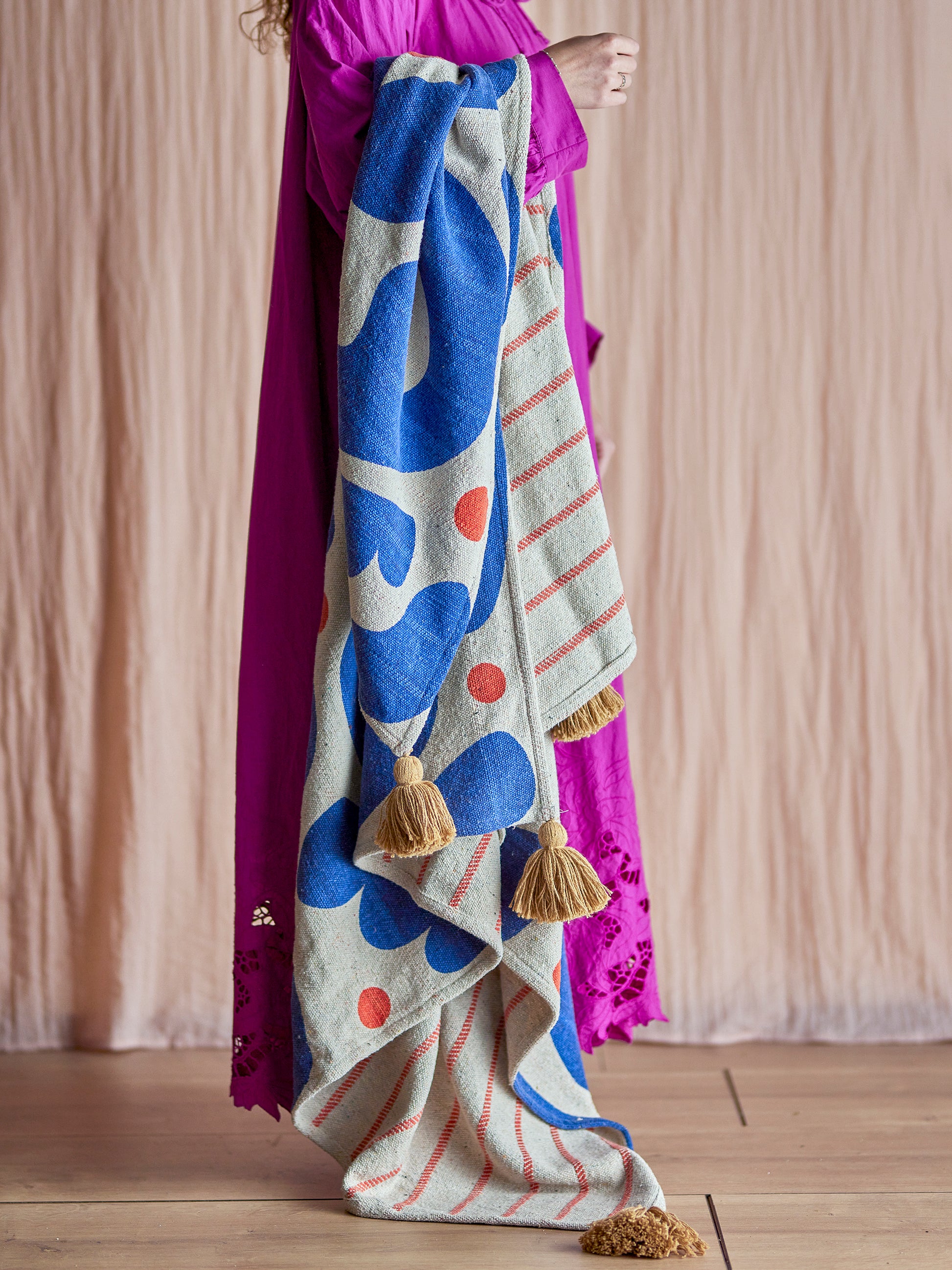 Colorful patterned blanket with tassels draped over a person wearing a purple garment.