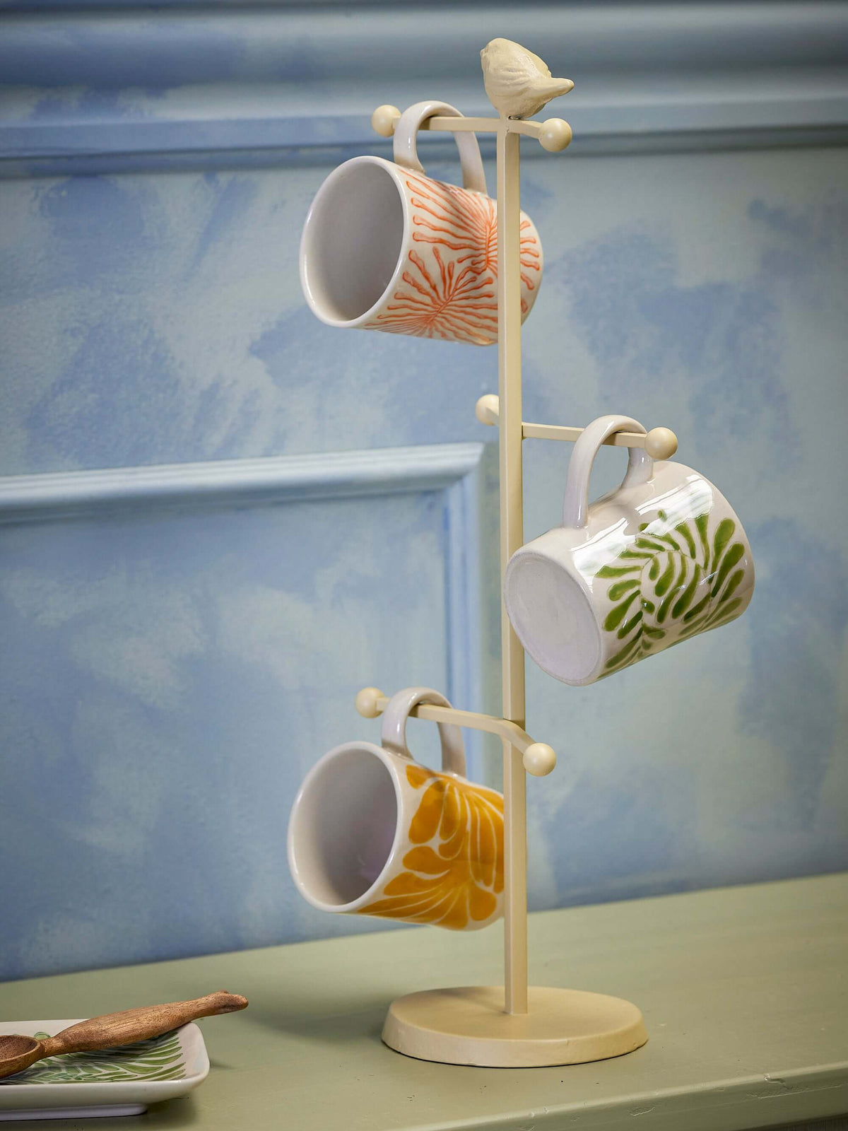 Mug tree with four mugs on a light blue wall background