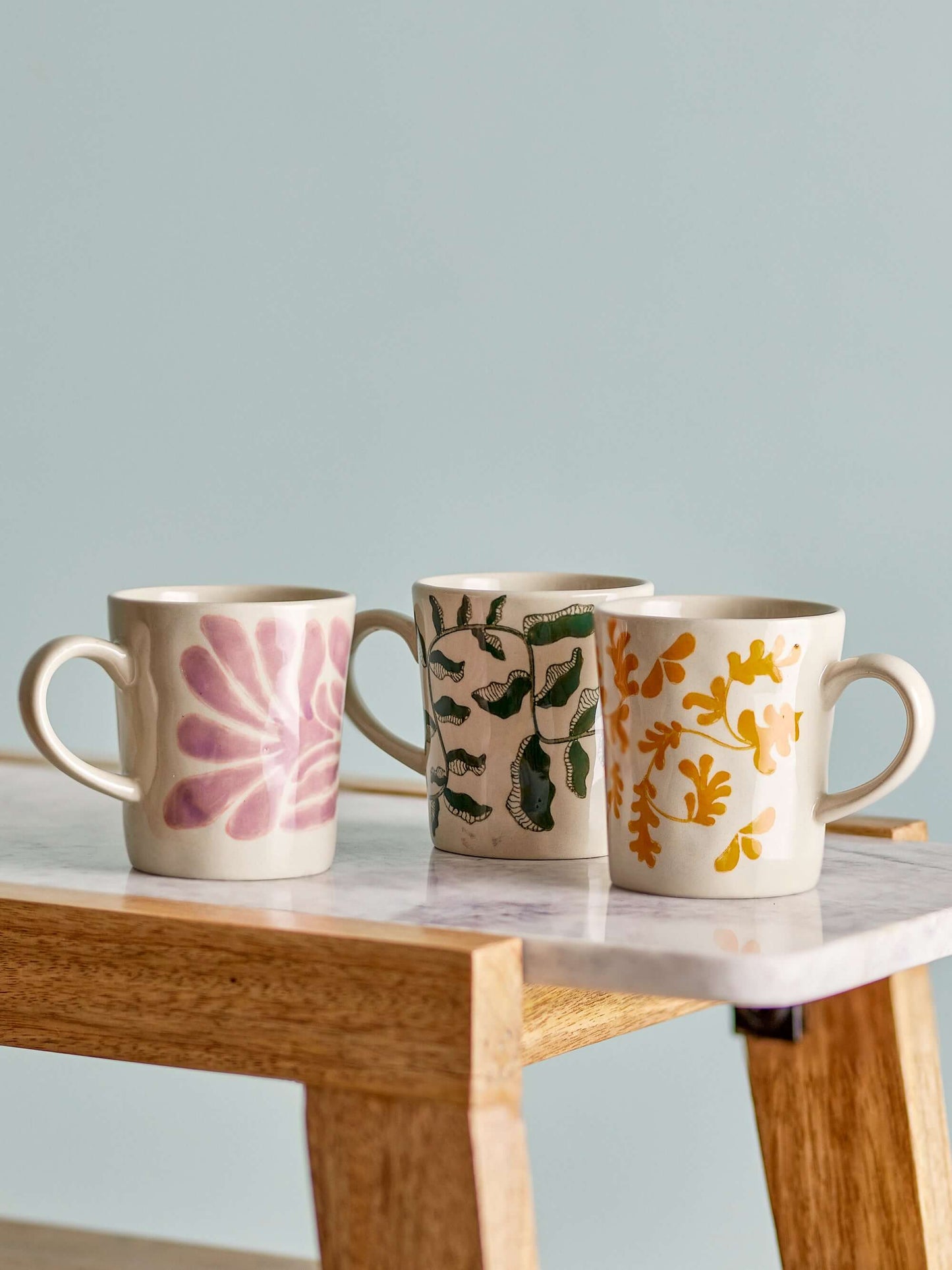 Three ceramic mugs with floral patterns on a wooden table against a light gray background