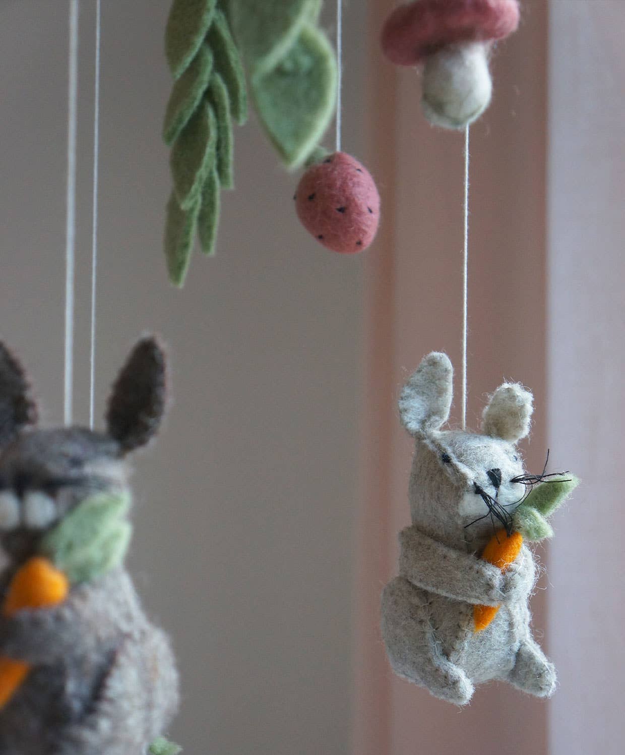 Felted animal toys hanging from strings against a neutral background