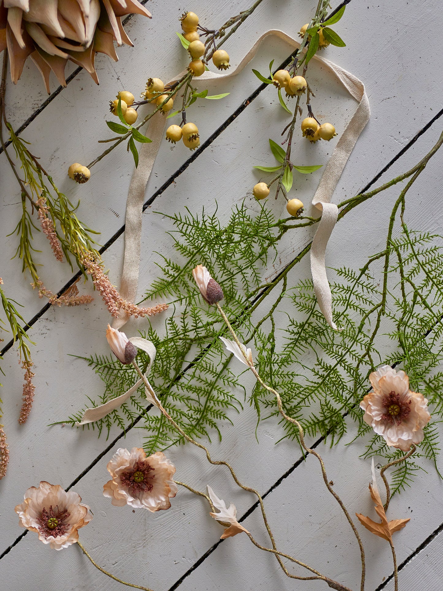 Decorative arrangement of greenery, flowers, and ribbons on a textured surface