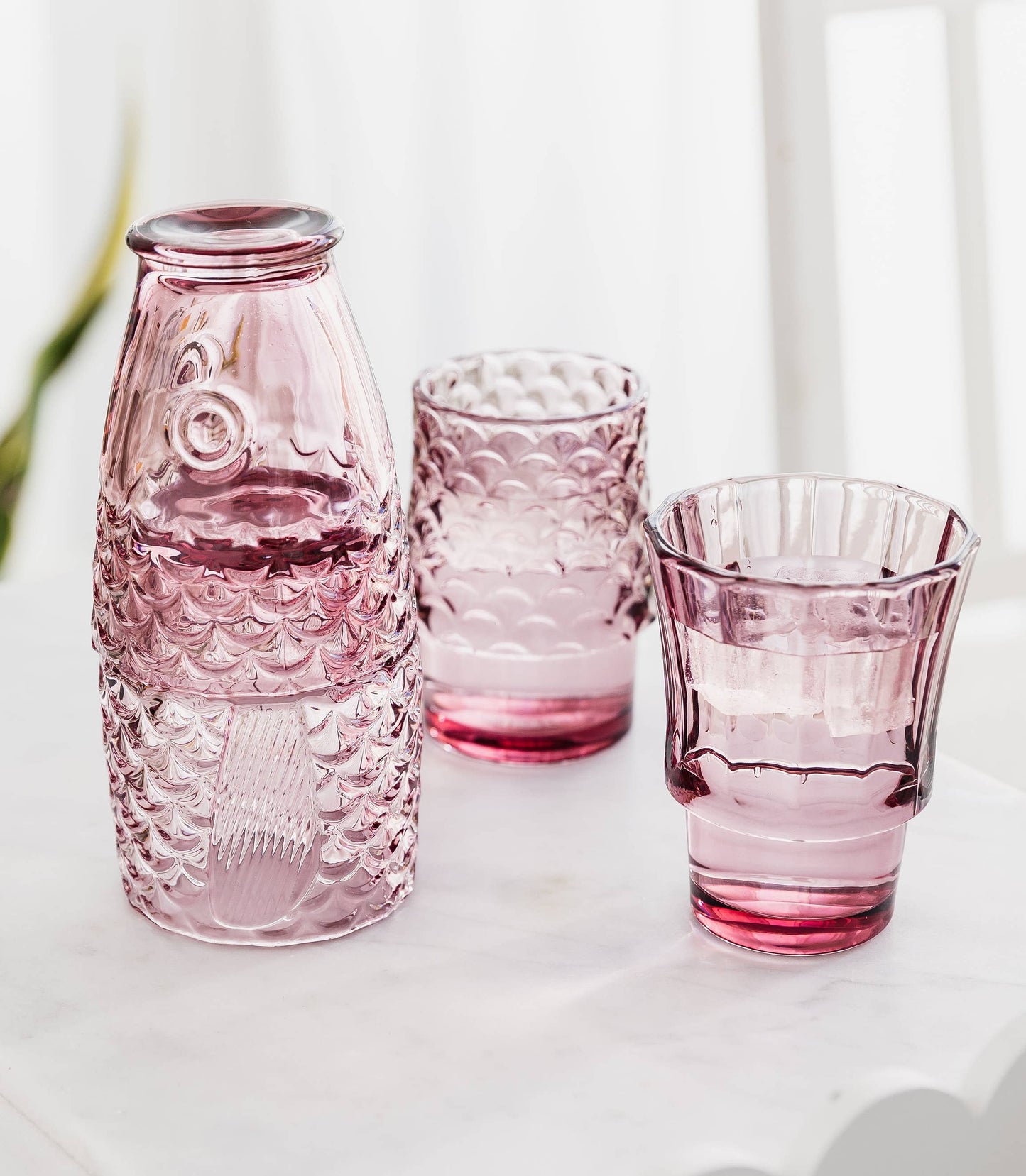Set of pink glass bottles and glasses on a white surface