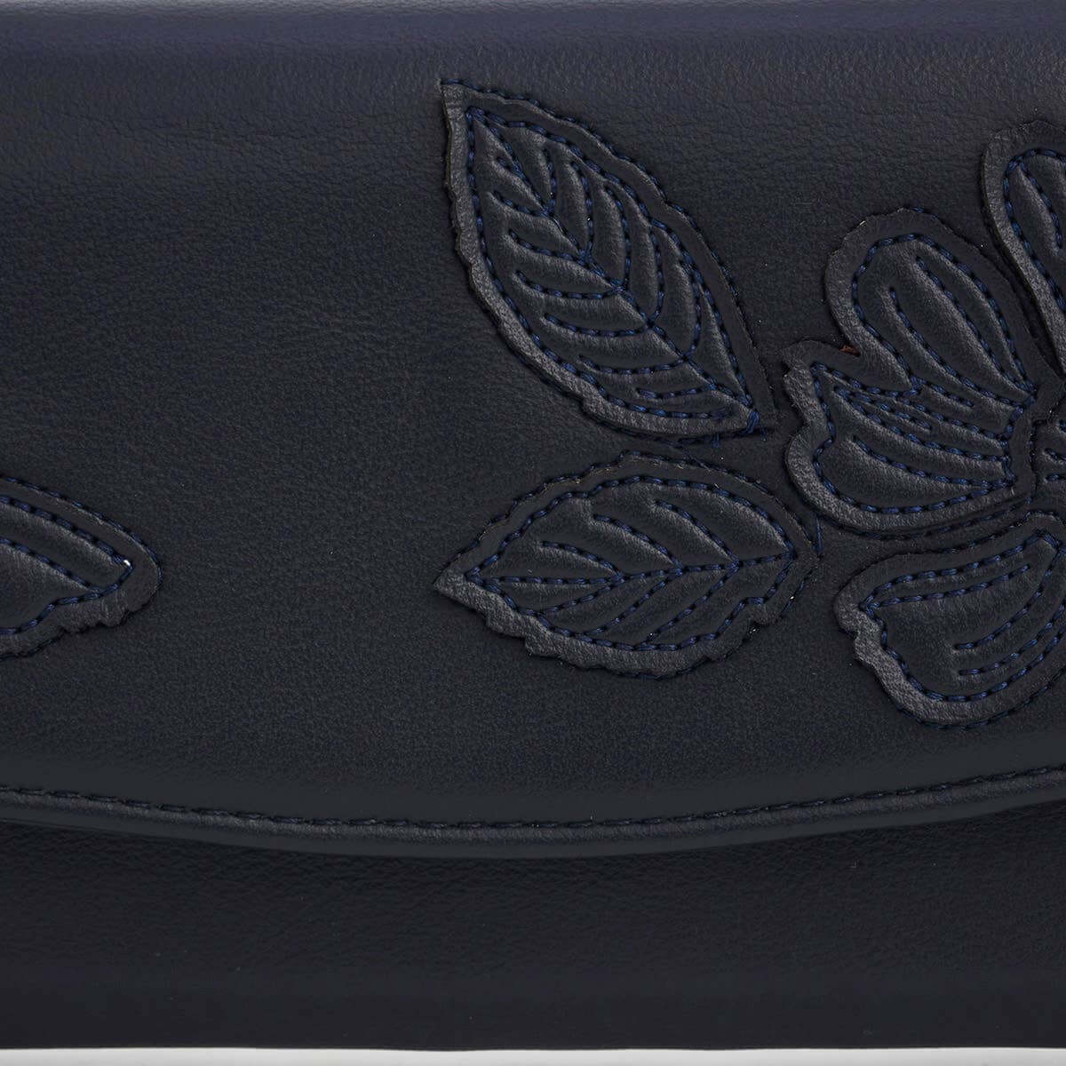 Close-up of a dark navy blue leather clutch featuring an embossed floral and leaf pattern with matching contrast stitching.