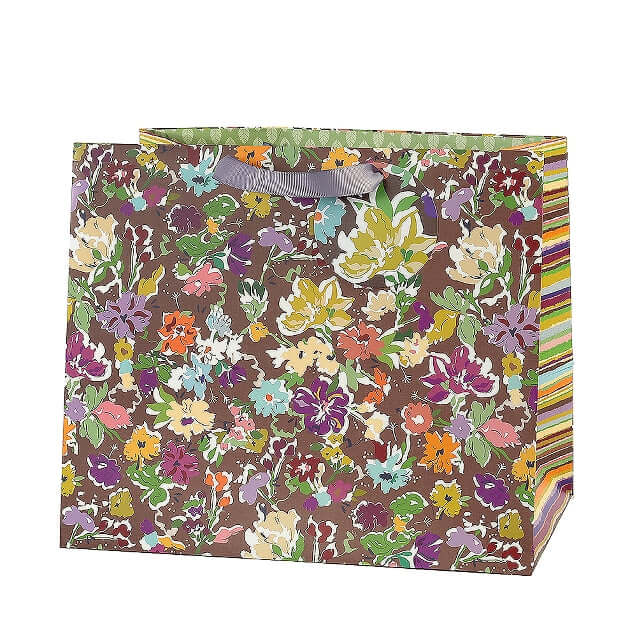 A square paper gift bag with a brown background covered in a dense multicolor floral print, featuring a gray ribbon handle and striped multicolor side panels.
