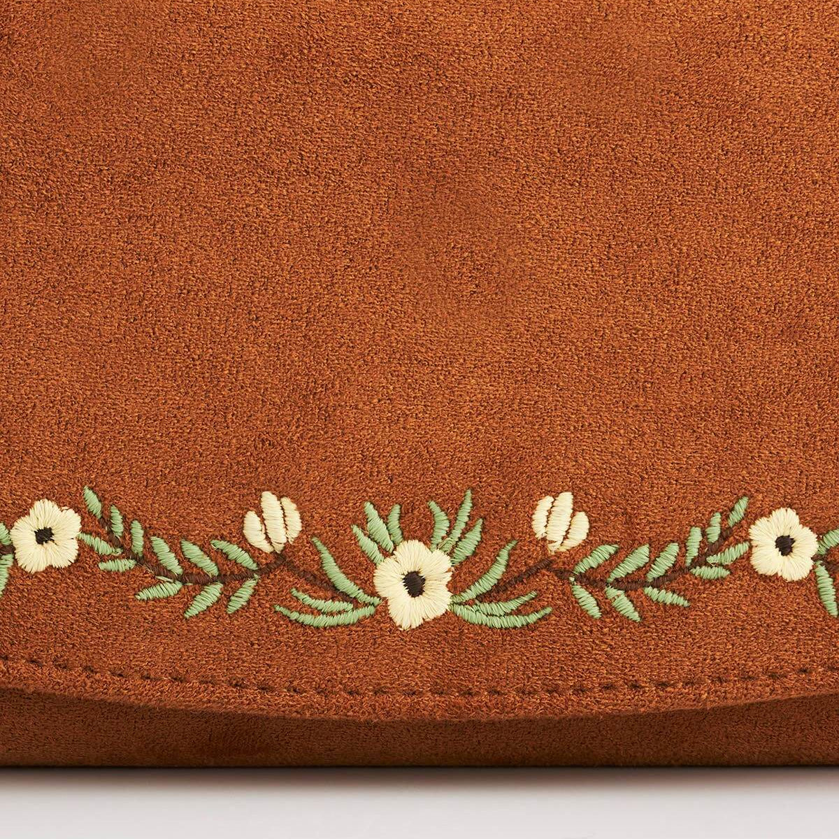Close-up of a brown suede or faux-suede item with a horizontal embroidered floral border featuring cream flowers and green leaves on a white background.