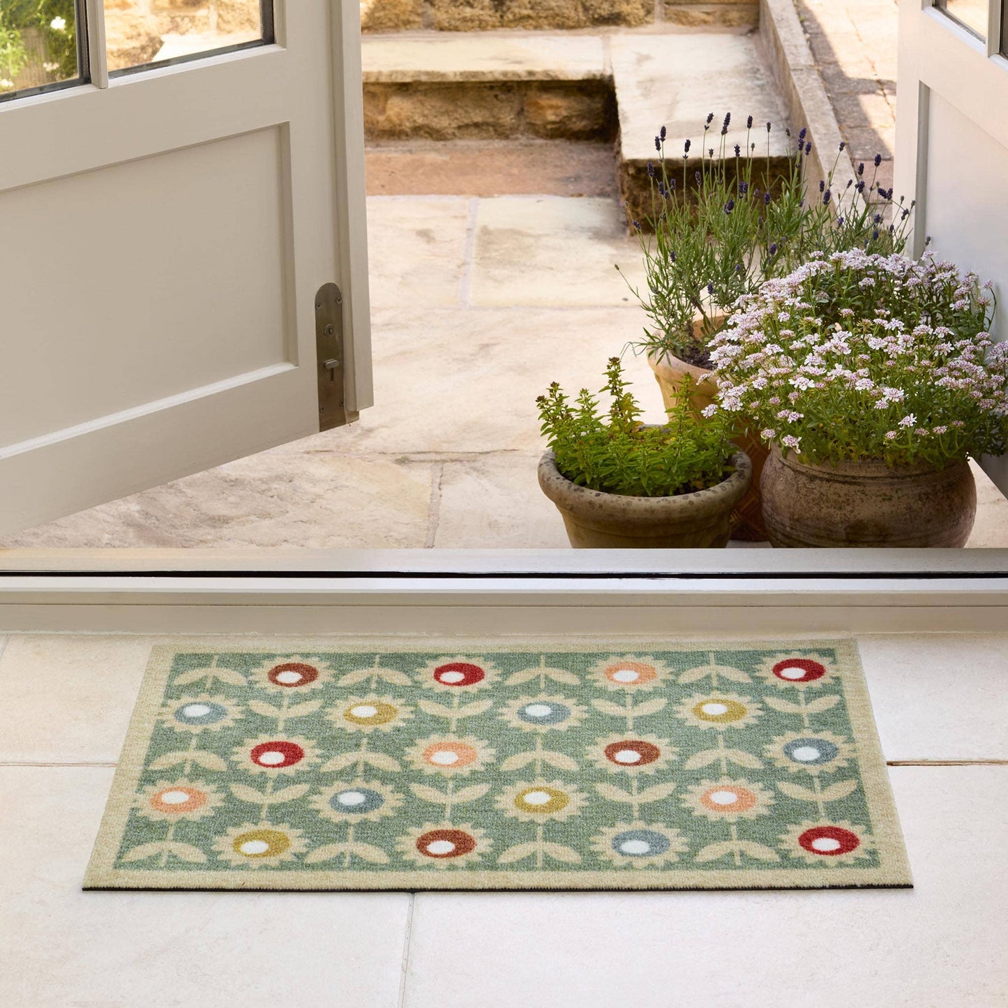 Decorative doormat with floral pattern on a light wooden floor, leading to a door.