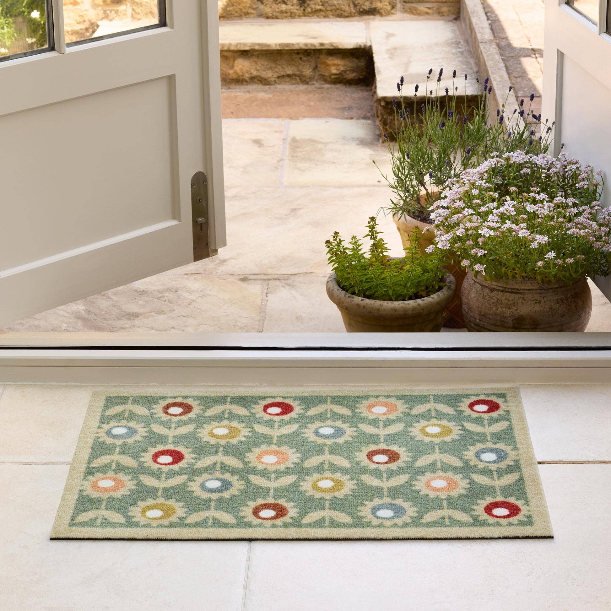 Decorative doormat with floral pattern on a light wooden floor, leading to a door.