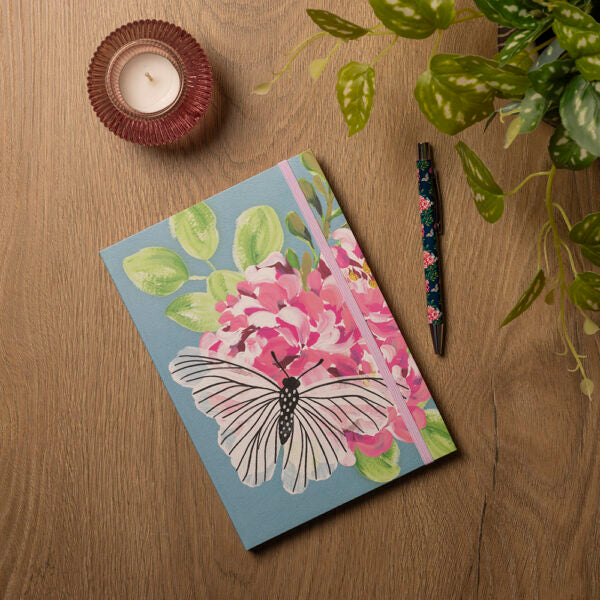Notebook with butterfly design on a wooden surface with a candle and plant.