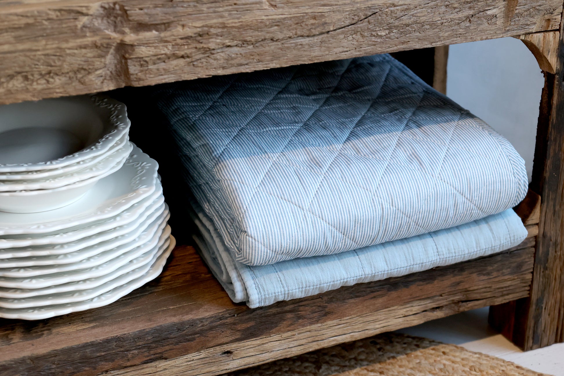 Stack of folded blue towels on a wooden surface with plates in the background