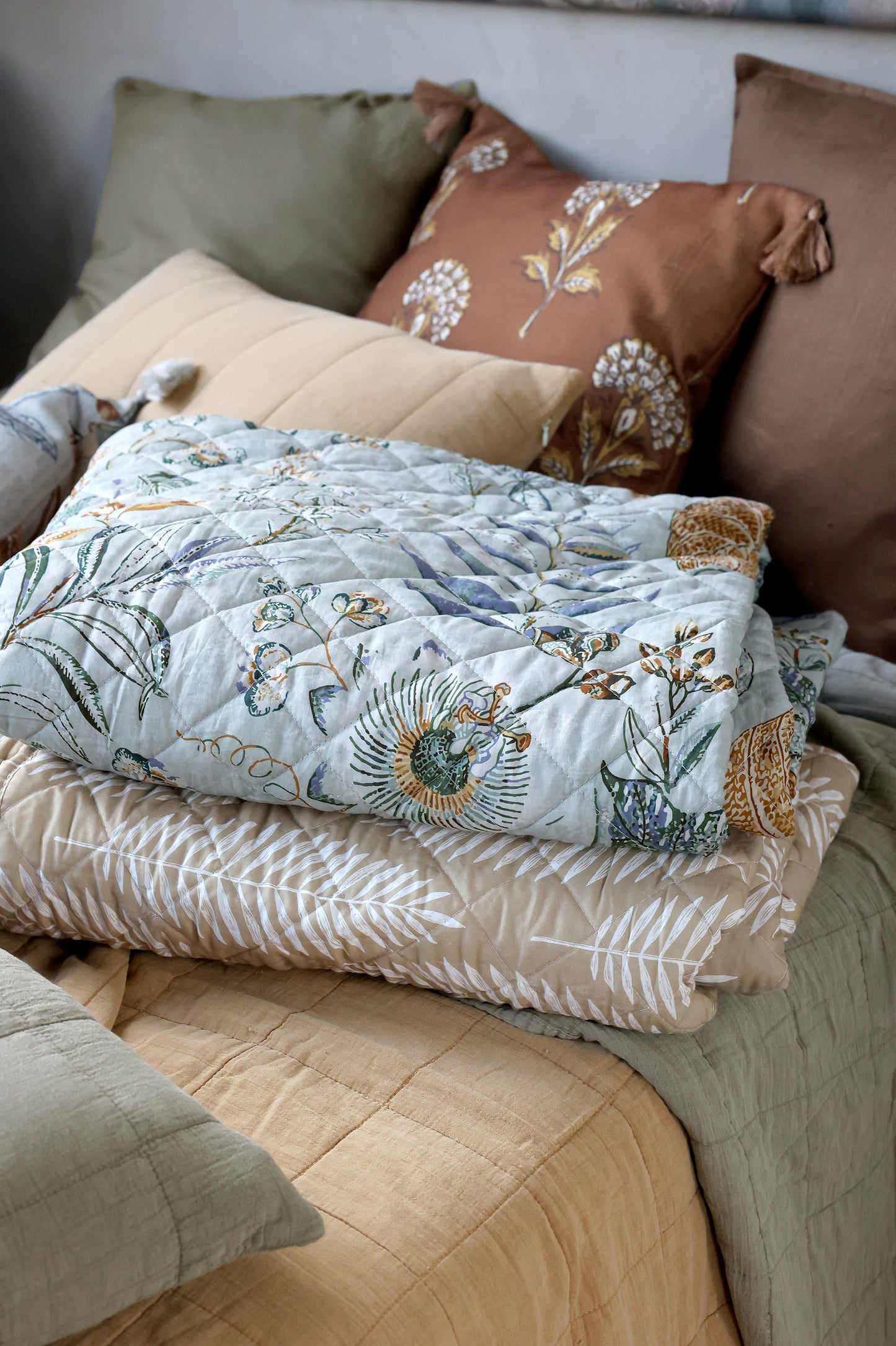 beige white tropical leaf quilt layered on a bed with decorative pillows
