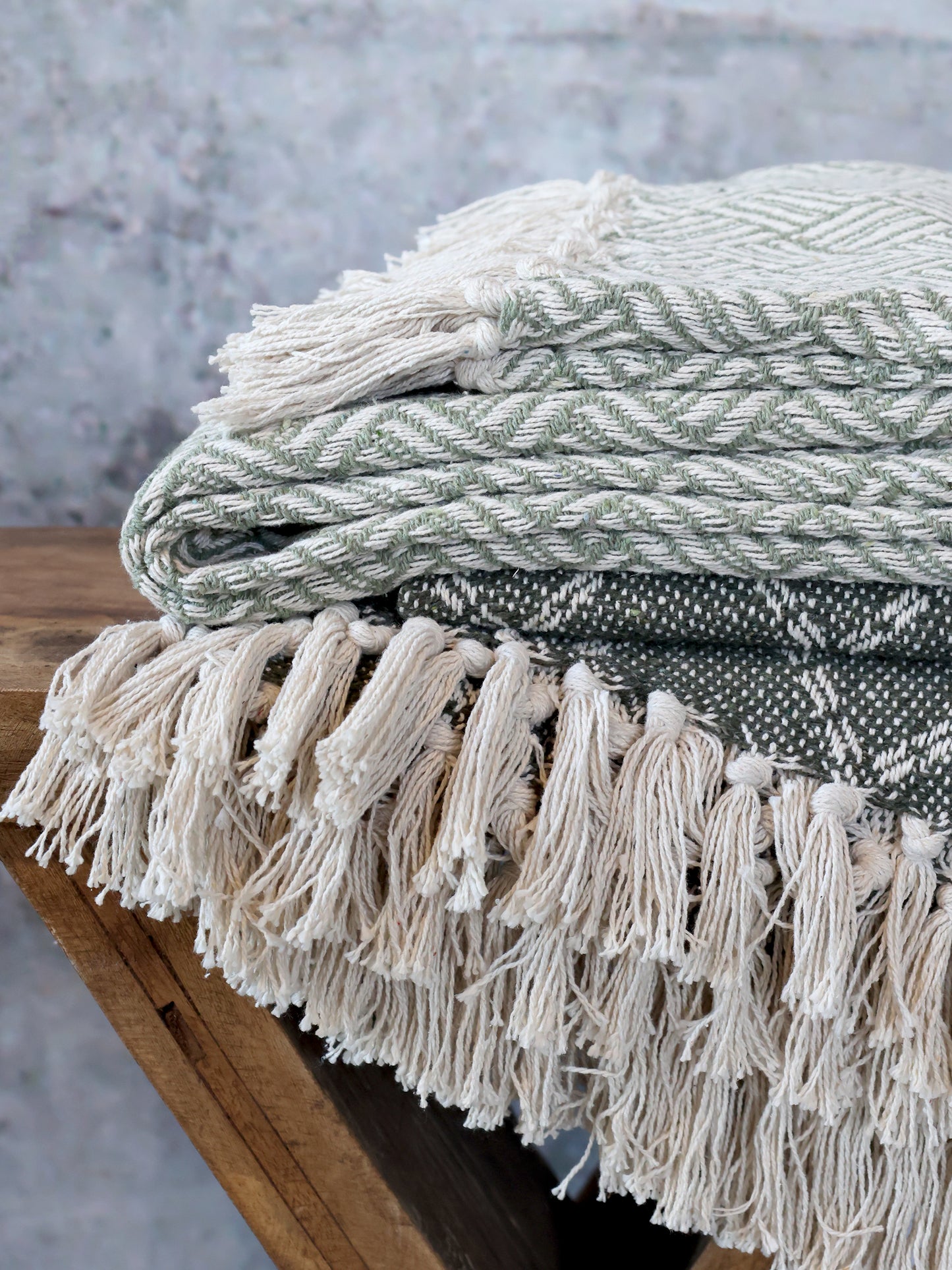 Textured blanket with tassels draped over a wooden surface against a gray background