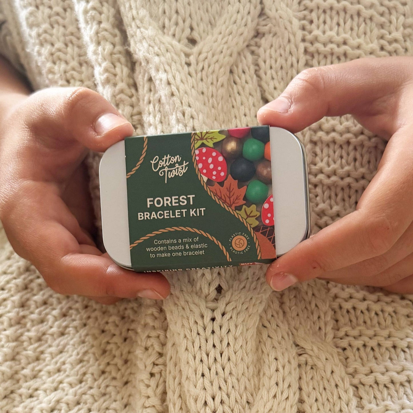 Cotton Twist Forest Bracelet Kit held by hands on a knitted fabric background