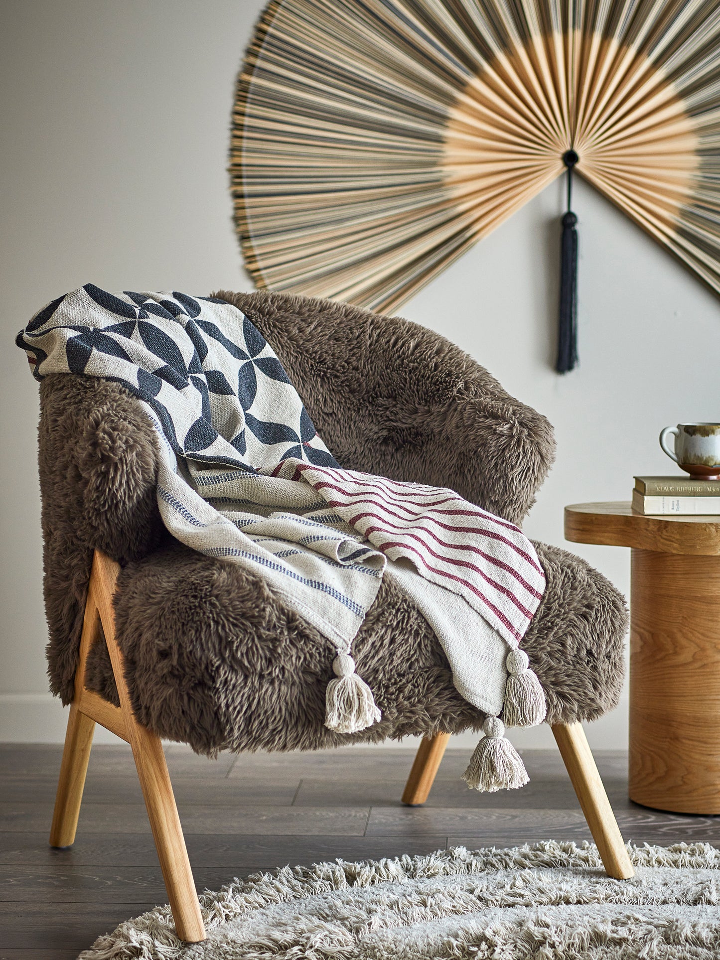 Brown armchair with patterned blanket, wooden side table, and decorative wall art.