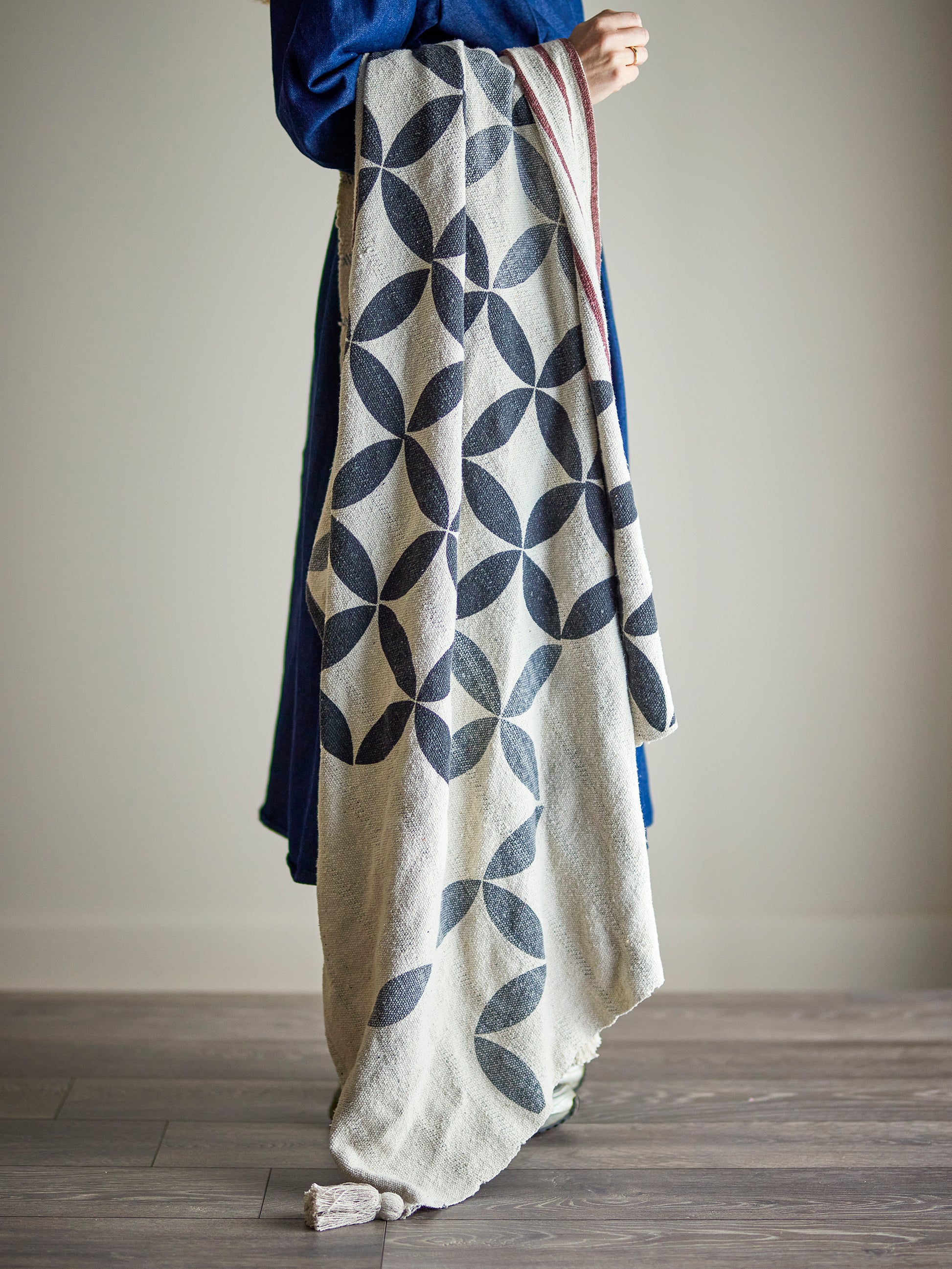 Person holding a patterned blanket with geometric design on a plain background