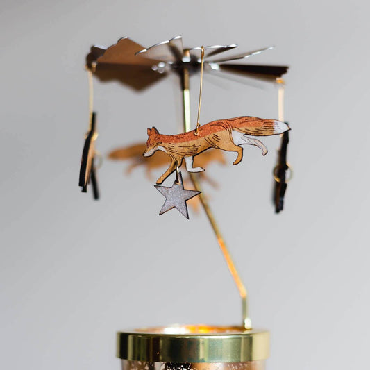 A decorative candle carousel featuring a fox and star design, with a glass votive and laser etched wooden ornaments in gold and black colors.