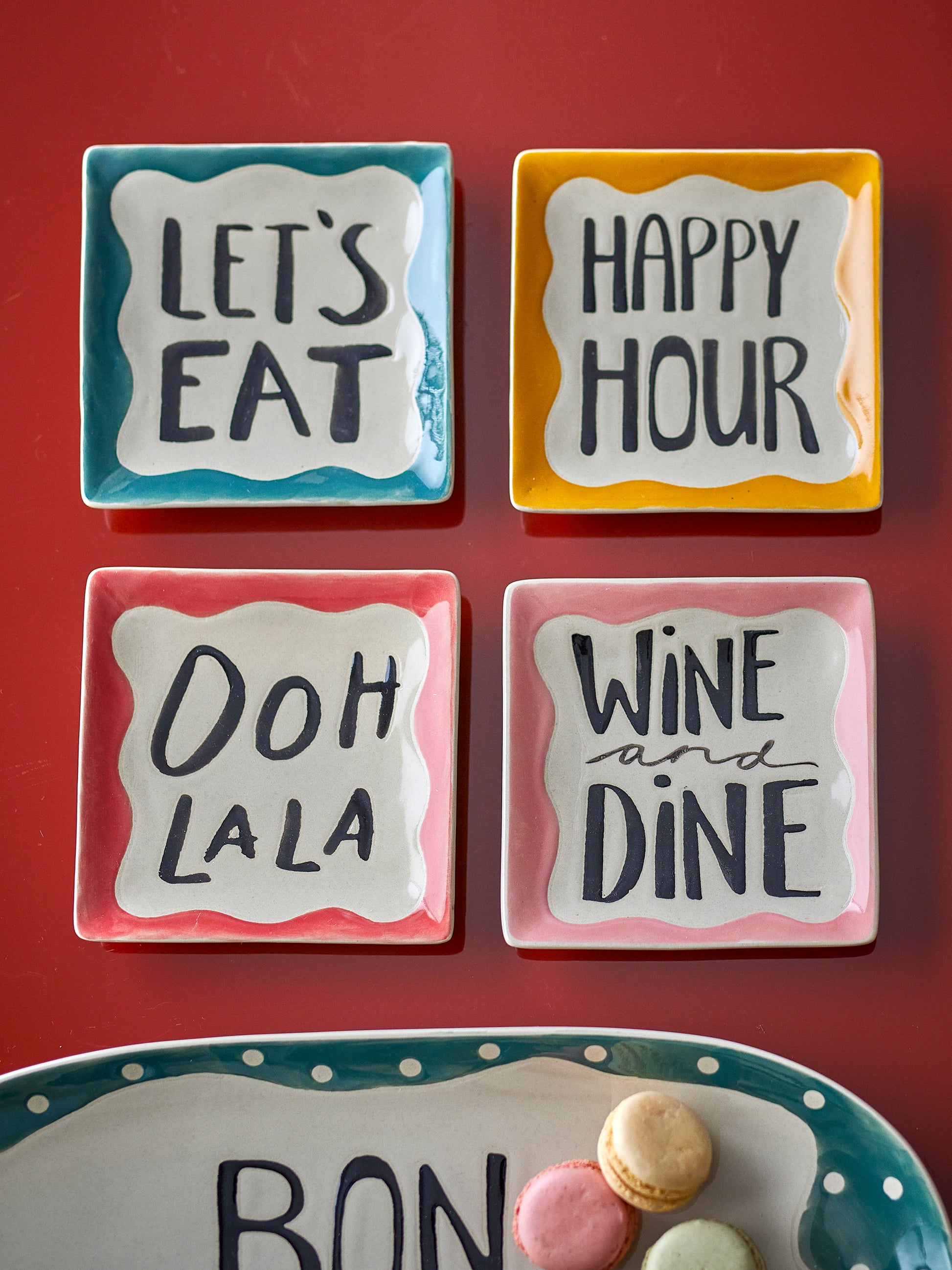 Four square ceramic plates with humorous sayings on a red background