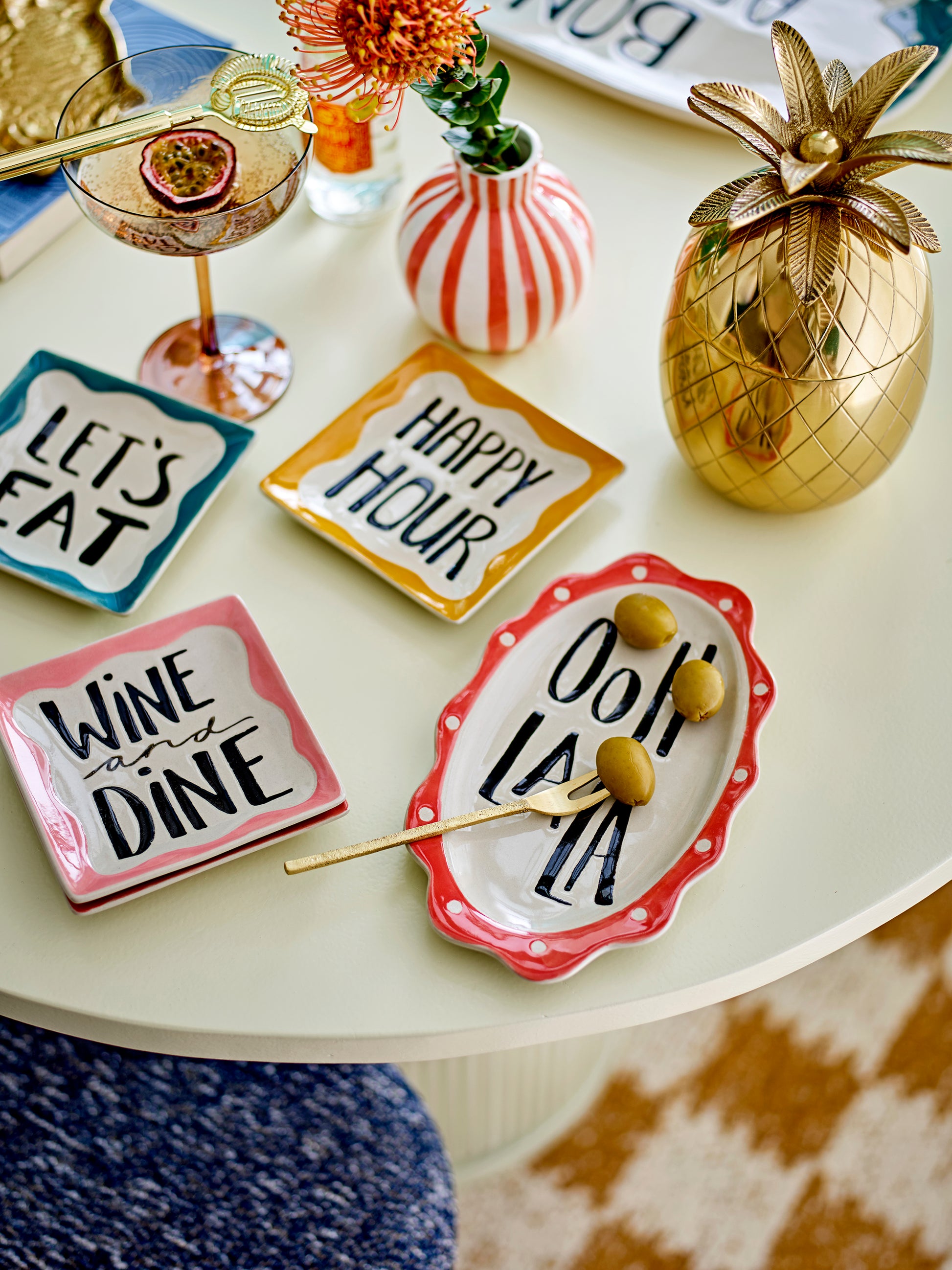Decorative plates with humorous sayings on a table with a pineapple and cocktail.
