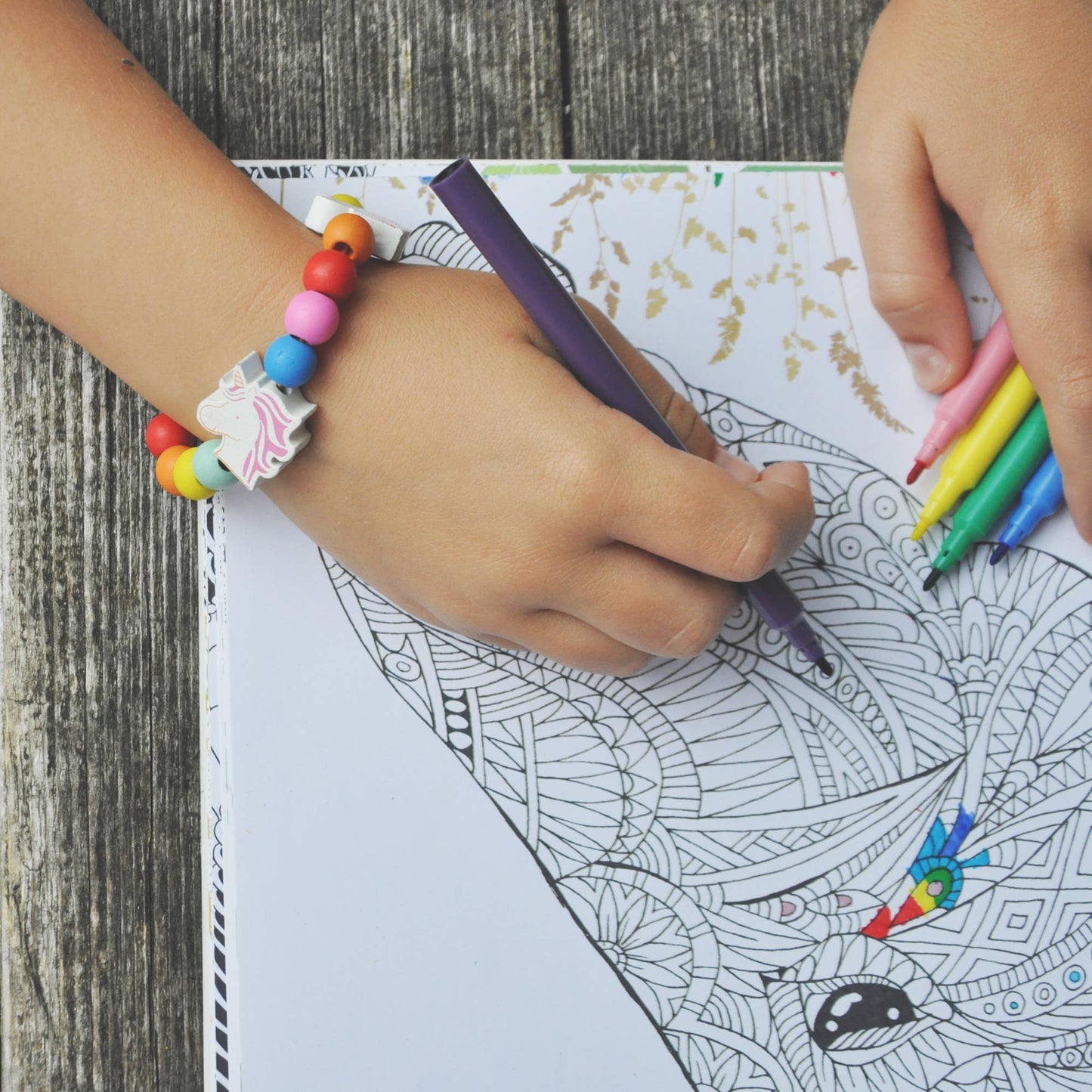 Child coloring a detailed design with colorful markers on a wooden surface