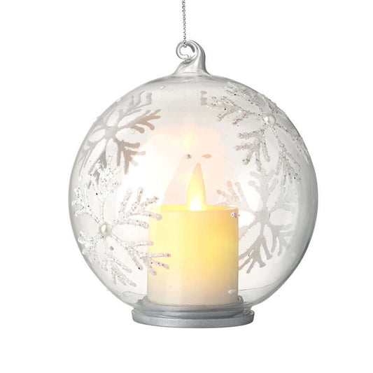 Decorative glass ball with snowflake patterns containing a lit candle on a white background