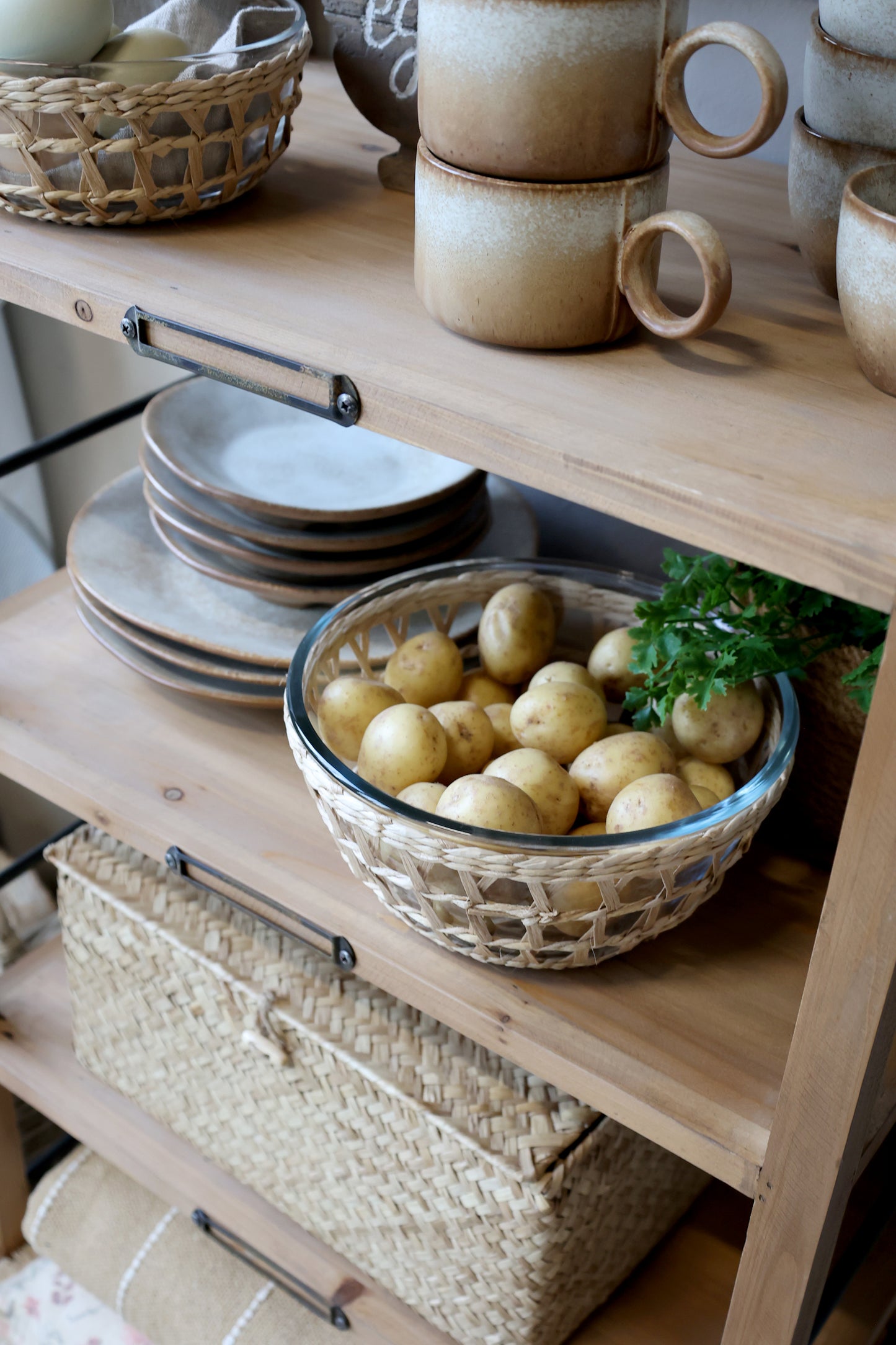 Wooden shelf with ceramic bowls, plates, and a basket of potatoes.