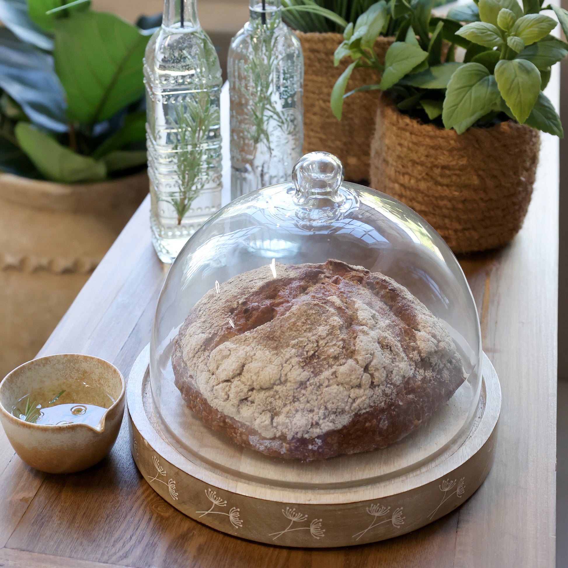 Bread under a glass dome on a wooden table with plants in the background