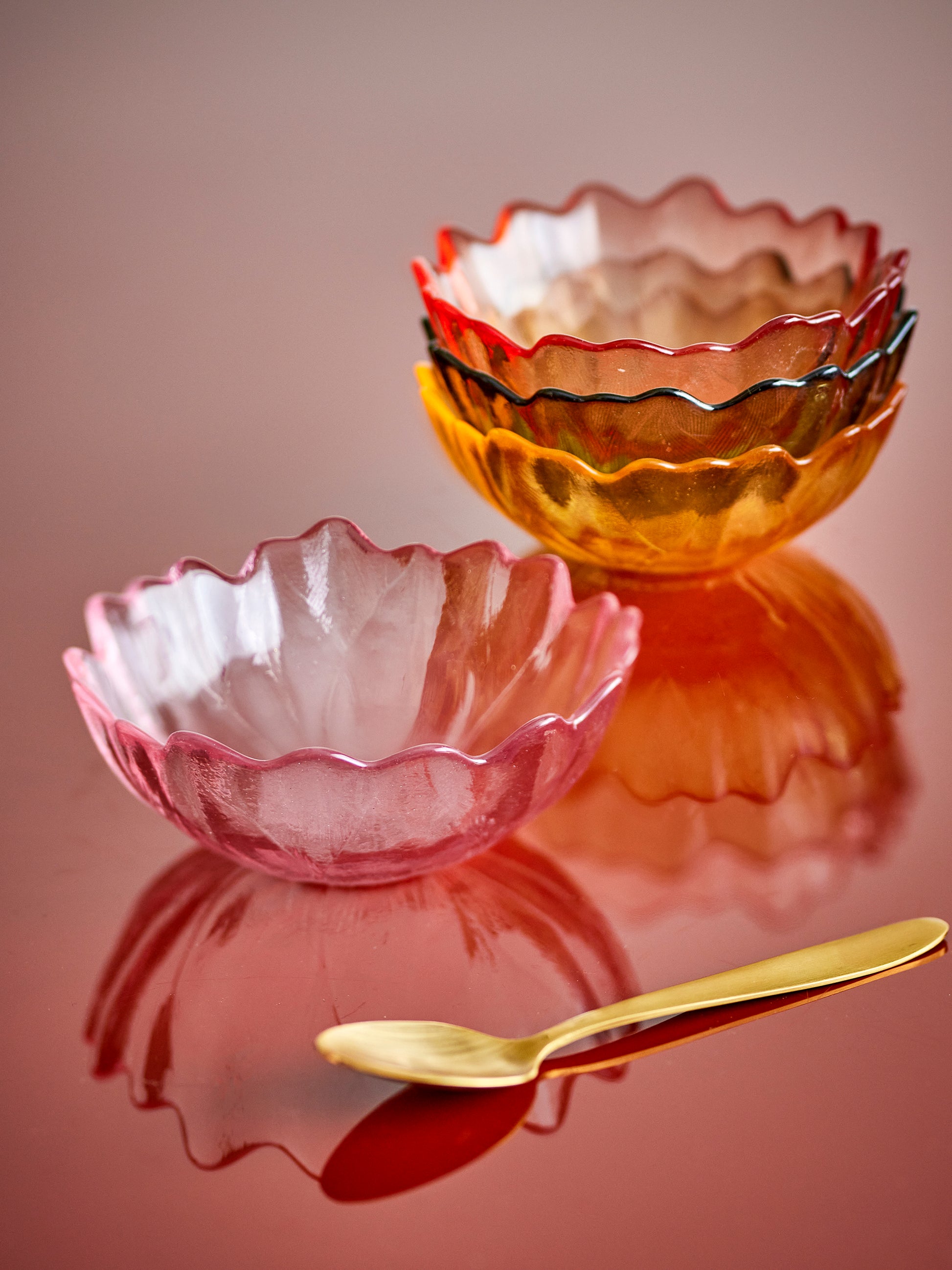 Set of colorful glass bowls with a gold spoon on a reflective surface